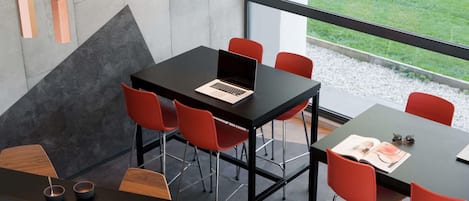 Une salle de réunion moderne, avec un ordinateur portable posé sur une table, des chaises rouges et une vue sur l’extérieur.