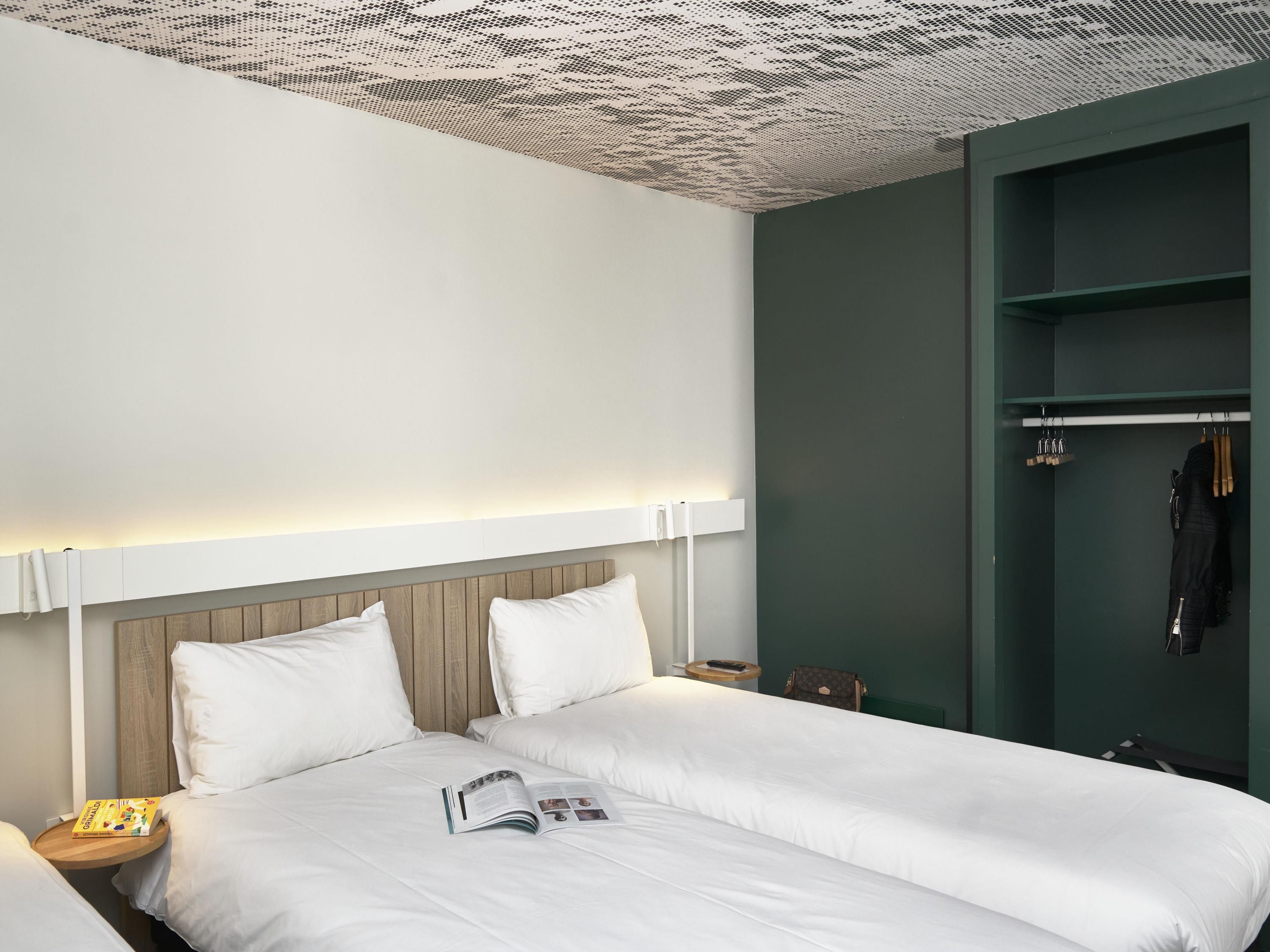 A hotel room with a bed, bedside tables, a wardrobe, and a ceiling with a unique pattern.