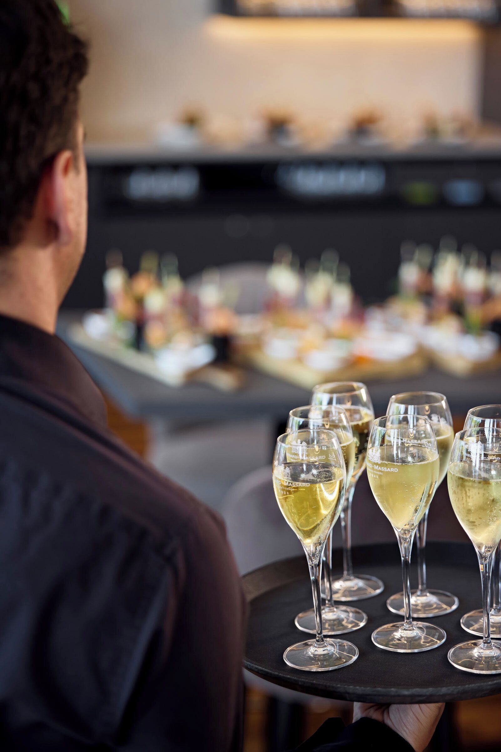 Une personne tenant un plateau sur lequel se trouvent plusieurs verres de vin blanc.
