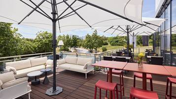 Une terrasse extérieure avec un canapé, des tables et des chaises, une rambarde et une vue sur les environs.