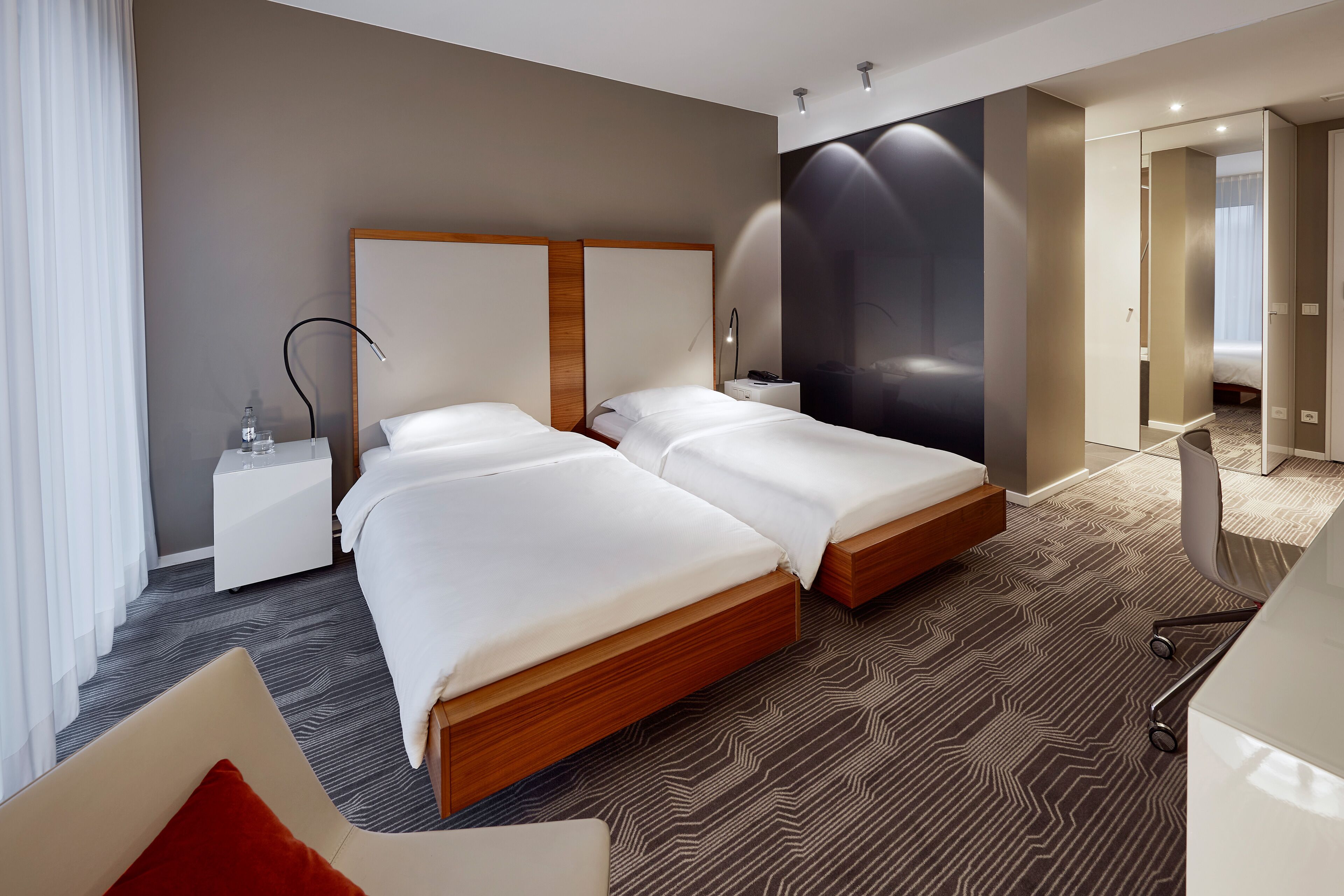 Ein modernes Hotelzimmer mit zwei Betten, einem Schreibtisch, einem Sessel und einer großen Wandmalerei.