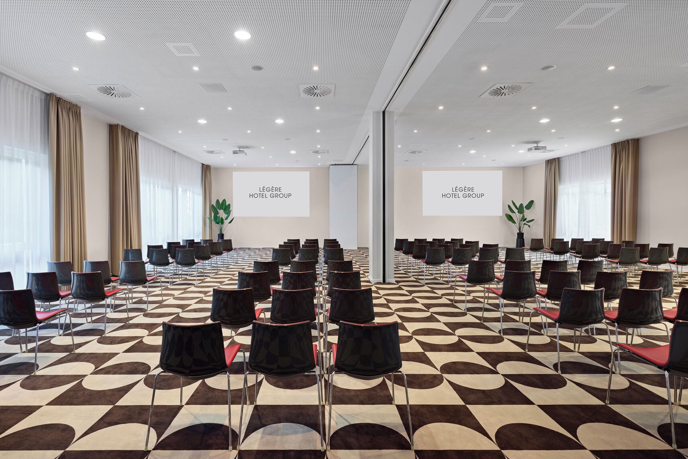 Un salón de conferencias con hileras de sillas, alfombra estampada e iluminación en el techo.