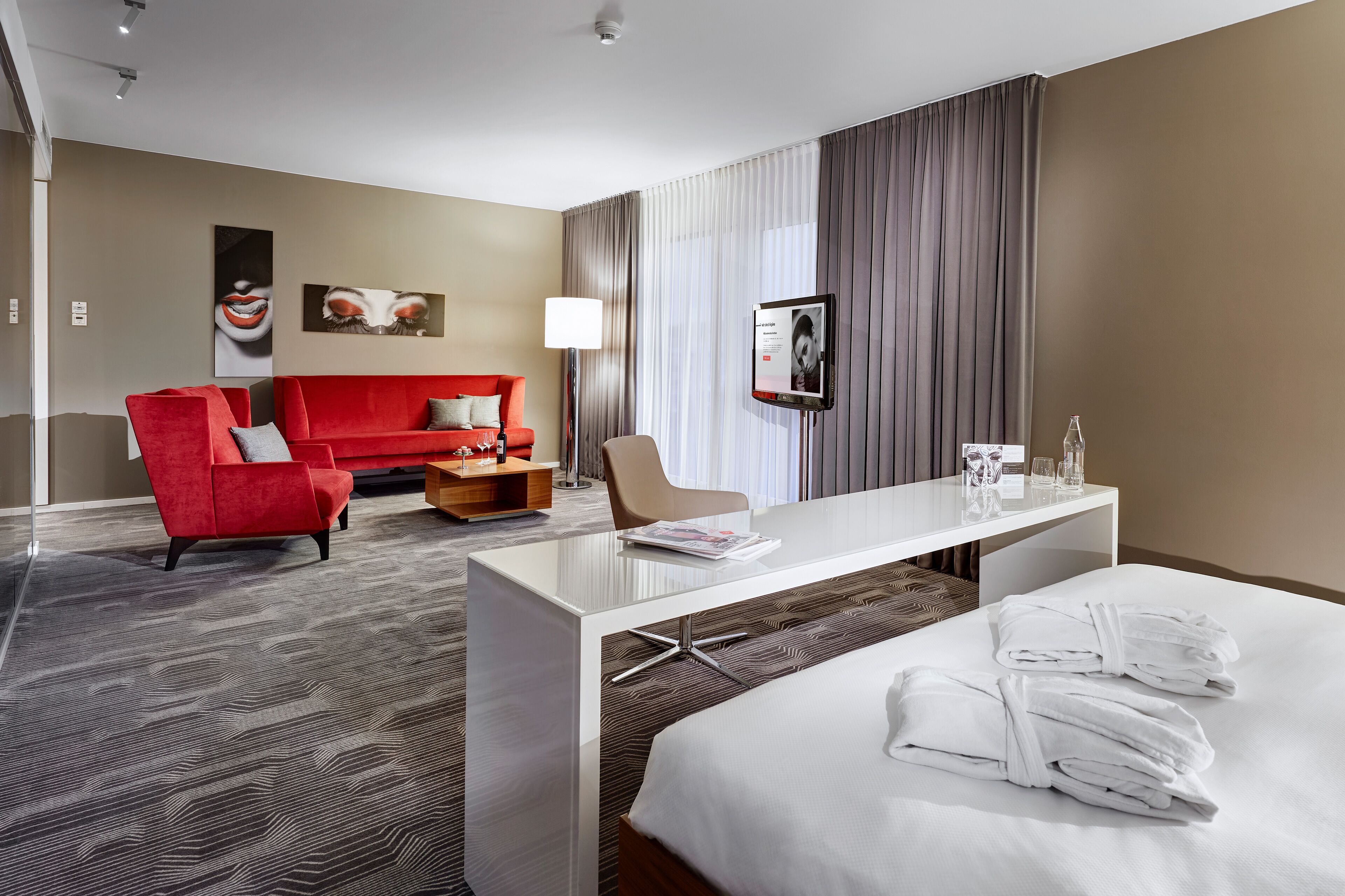 Una habitación de hotel con una cama, un sofá rojo, un escritorio blanco y un televisor.