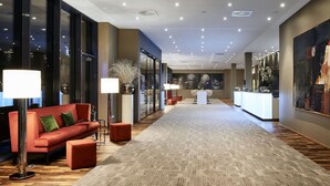 Un vestíbulo de hotel con un sofá rojo, lámparas de pie, una alfombra estampada y un mostrador de recepción.