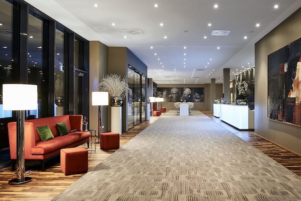 Un hall d’hôtel avec un canapé rouge, des lampadaires, une moquette à motifs et un comptoir d’accueil.
