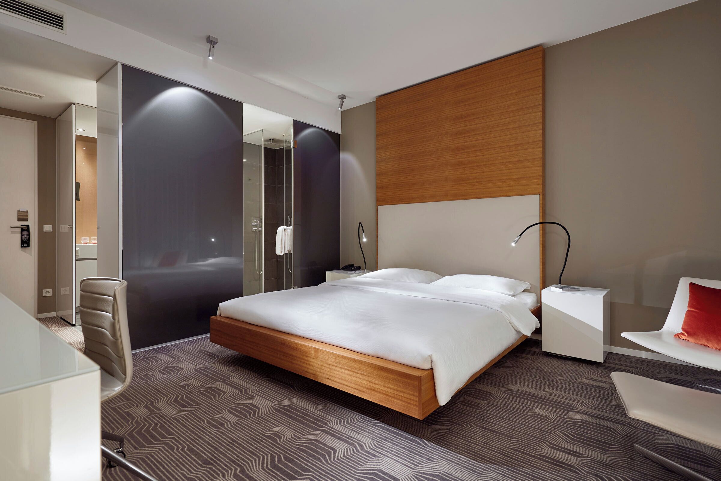 A modern hotel room with a large bed, a desk, a chair, and a shower area.