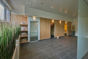 A modern hotel lobby with a large open space, a reception desk, and a glass door leading to the rooms.