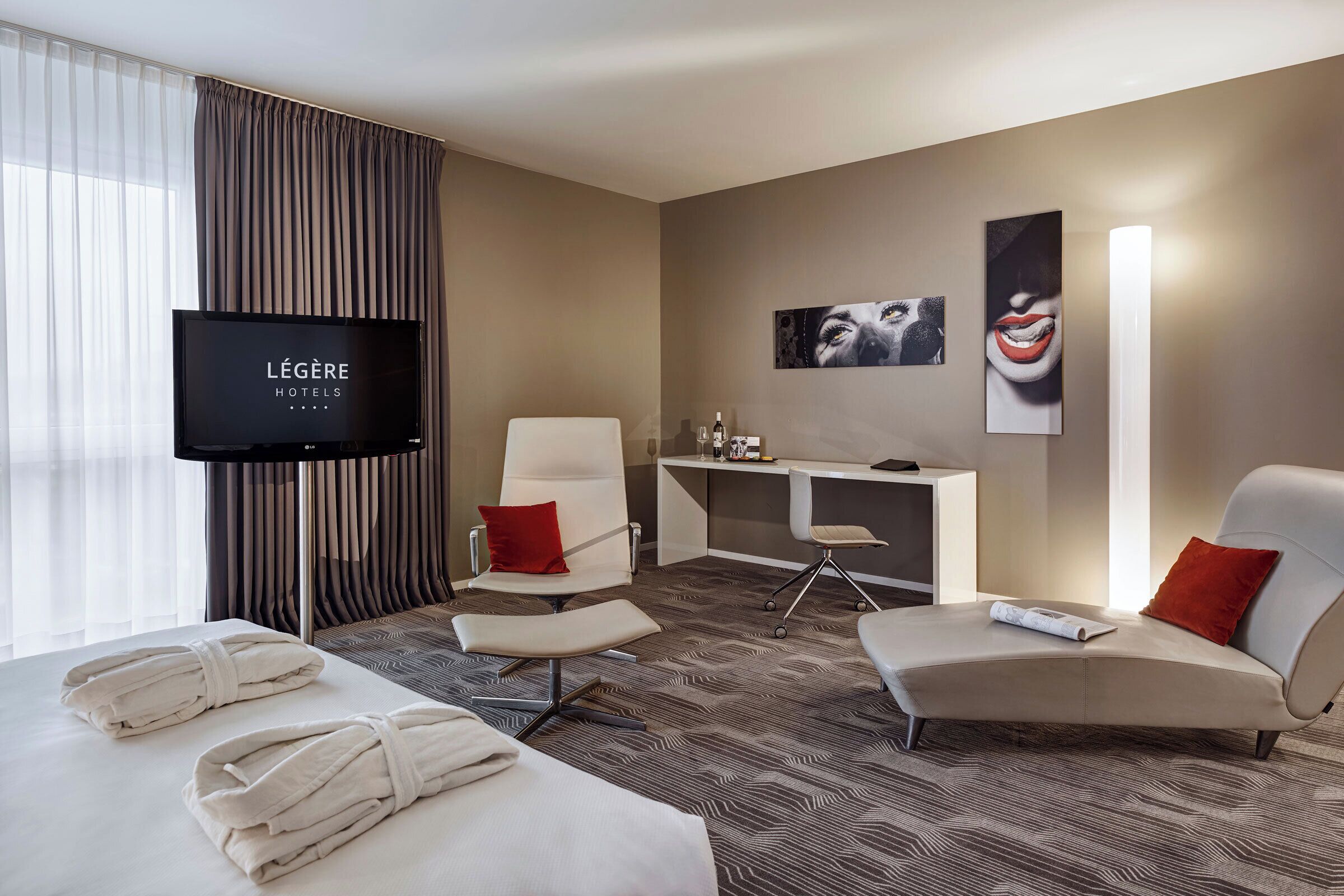 Ein Hotelzimmer mit Bett, zwei Sesseln, einem Schreibtisch, einem Fernseher und Bildern an der Wand.