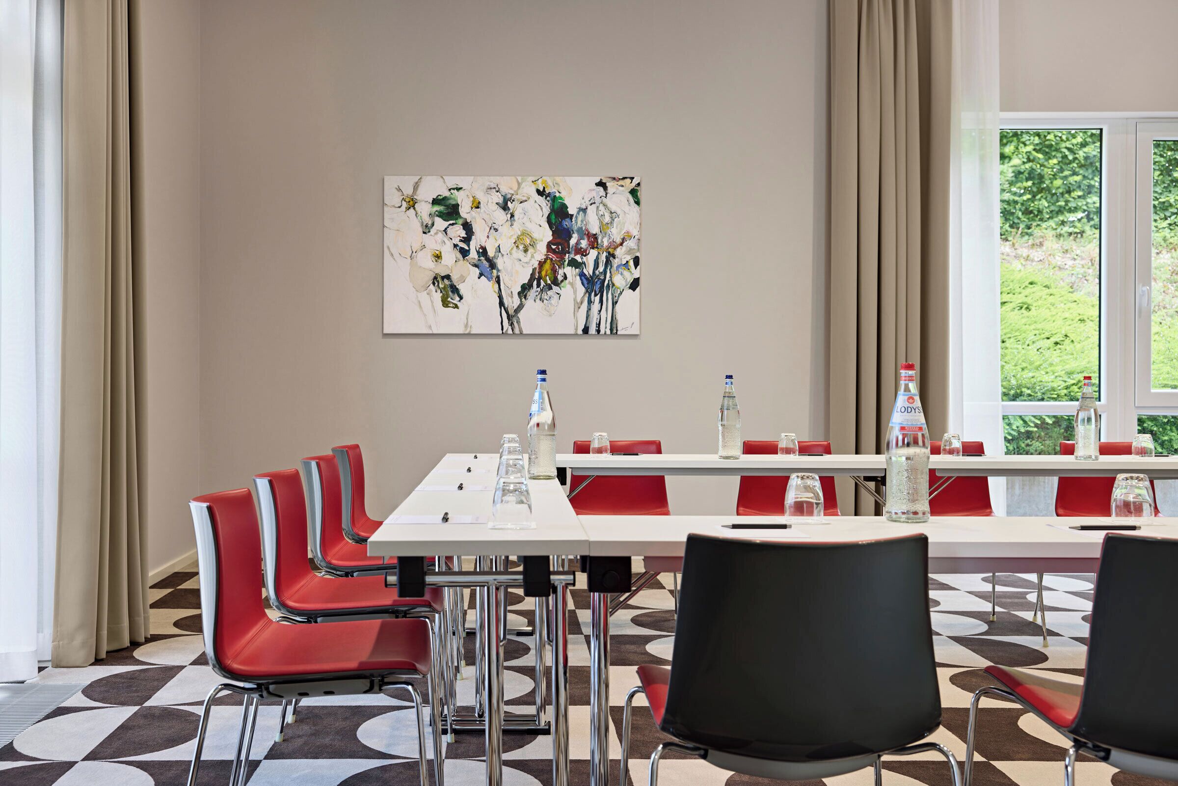 Een vergaderzaal met een lange tafel, rode stoelen en een schilderij aan de muur.