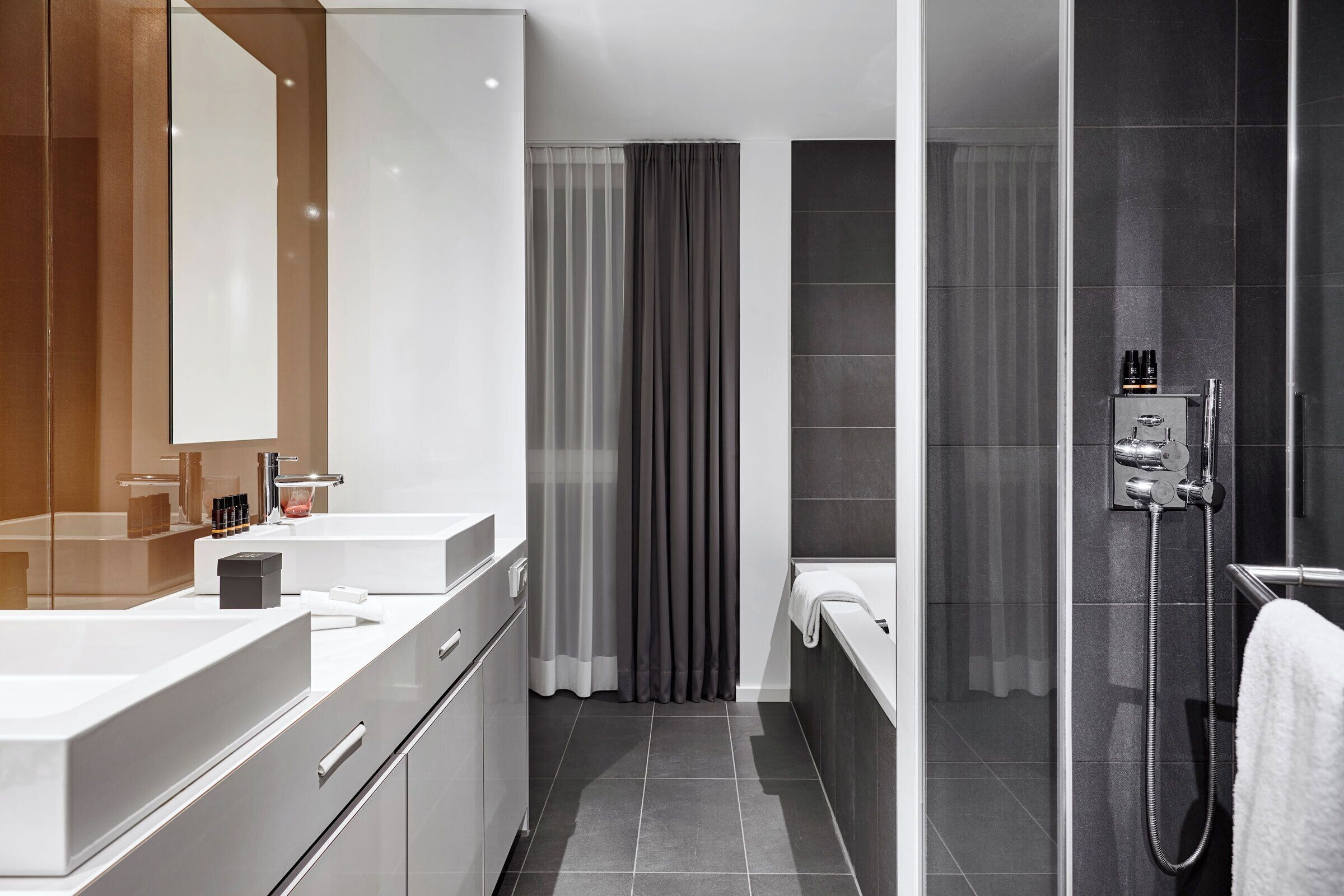 A modern bathroom with a large mirror, two sinks, a shower, and a toilet.