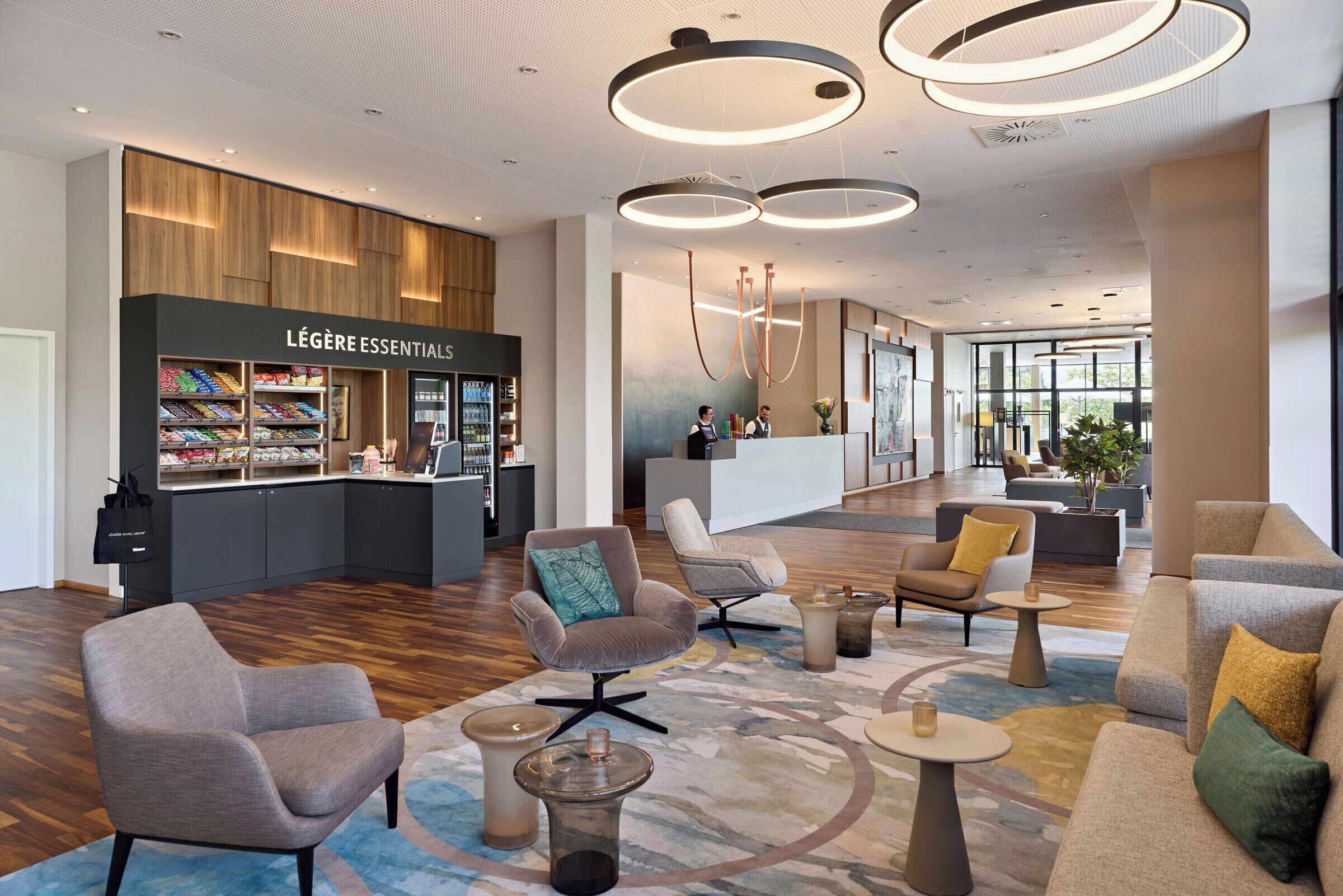 A modern hotel lobby with a Légère Essentials store, seating areas, and a reception desk.