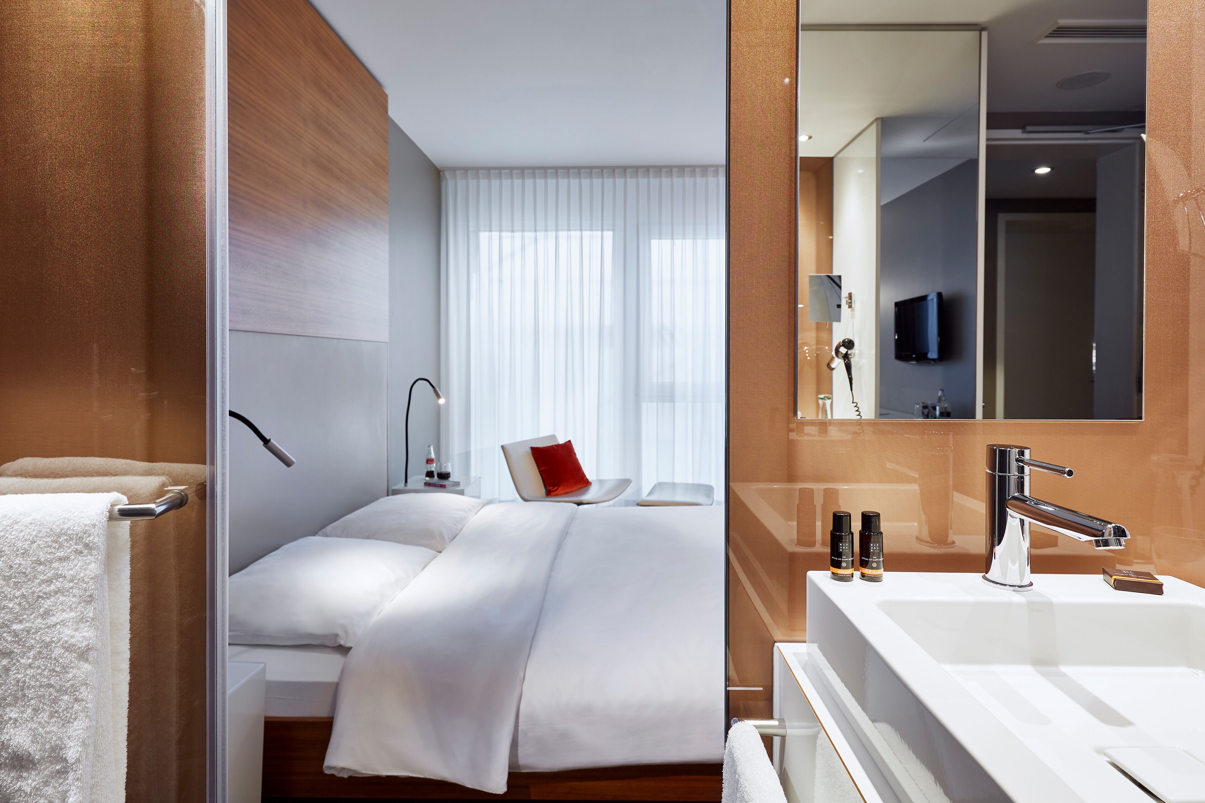 Ett modernt hotellrum med en stor säng, ett badrum med spegel och handfat samt en tv som är inbyggd i spegeln.