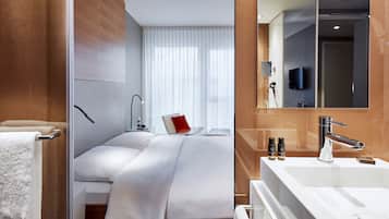 Ett modernt hotellrum med en stor säng, ett badrum med spegel och handfat samt en tv som är inbyggd i spegeln.