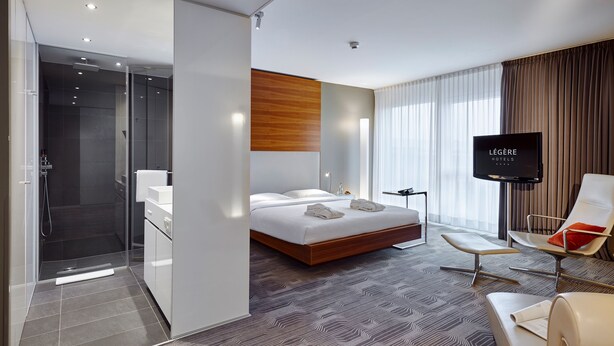 Una habitación de hotel moderna con una cama grande, televisión, zona de estar y ducha.