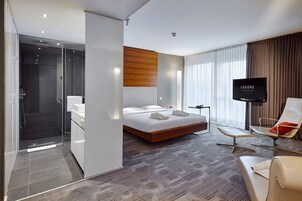 Une chambre d’hôtel moderne dotée d’un grand lit, d’une télévision, d’un coin salon et d’une douche.