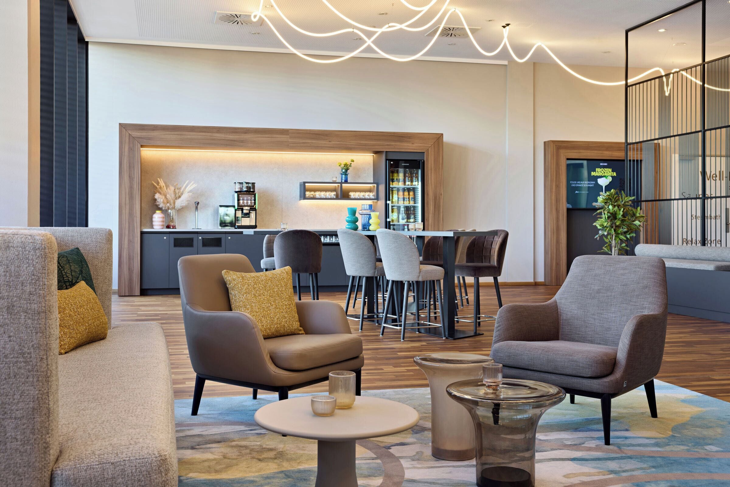 A modern lounge area with sofas, a coffee table, and a bar area in the background.