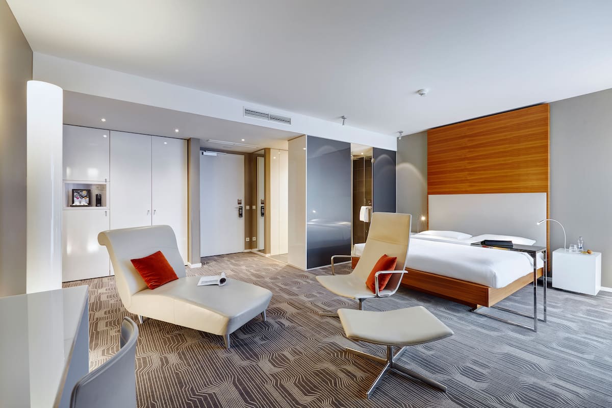 Ein modernes Hotelzimmer mit Bett, zwei Sessel, einem Schreibtisch und einem Kleiderschrank.