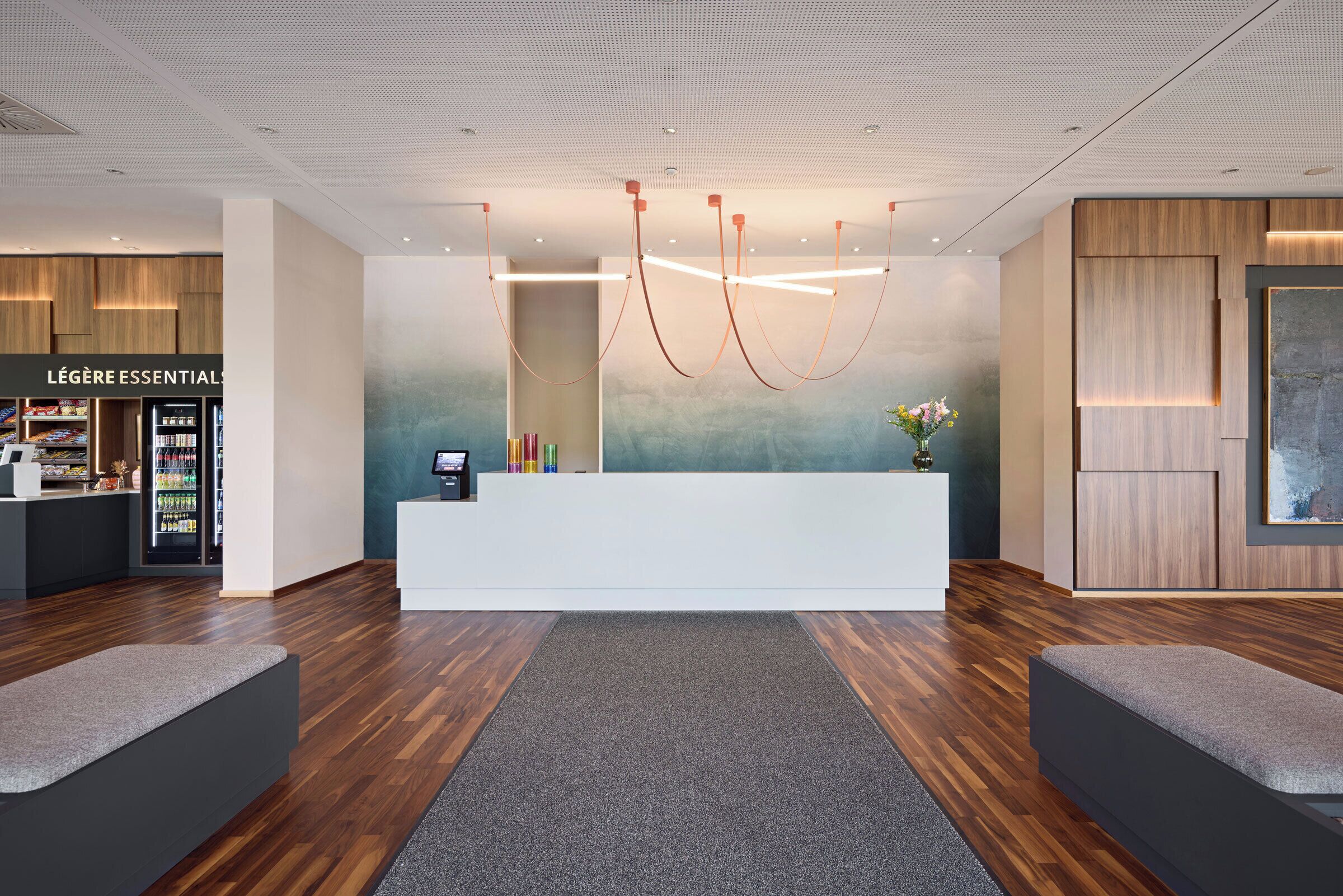 Un comptoir d’accueil moderne doté d’un écran numérique, un comptoir d’accueil en bois et un luminaire fixé au mur.