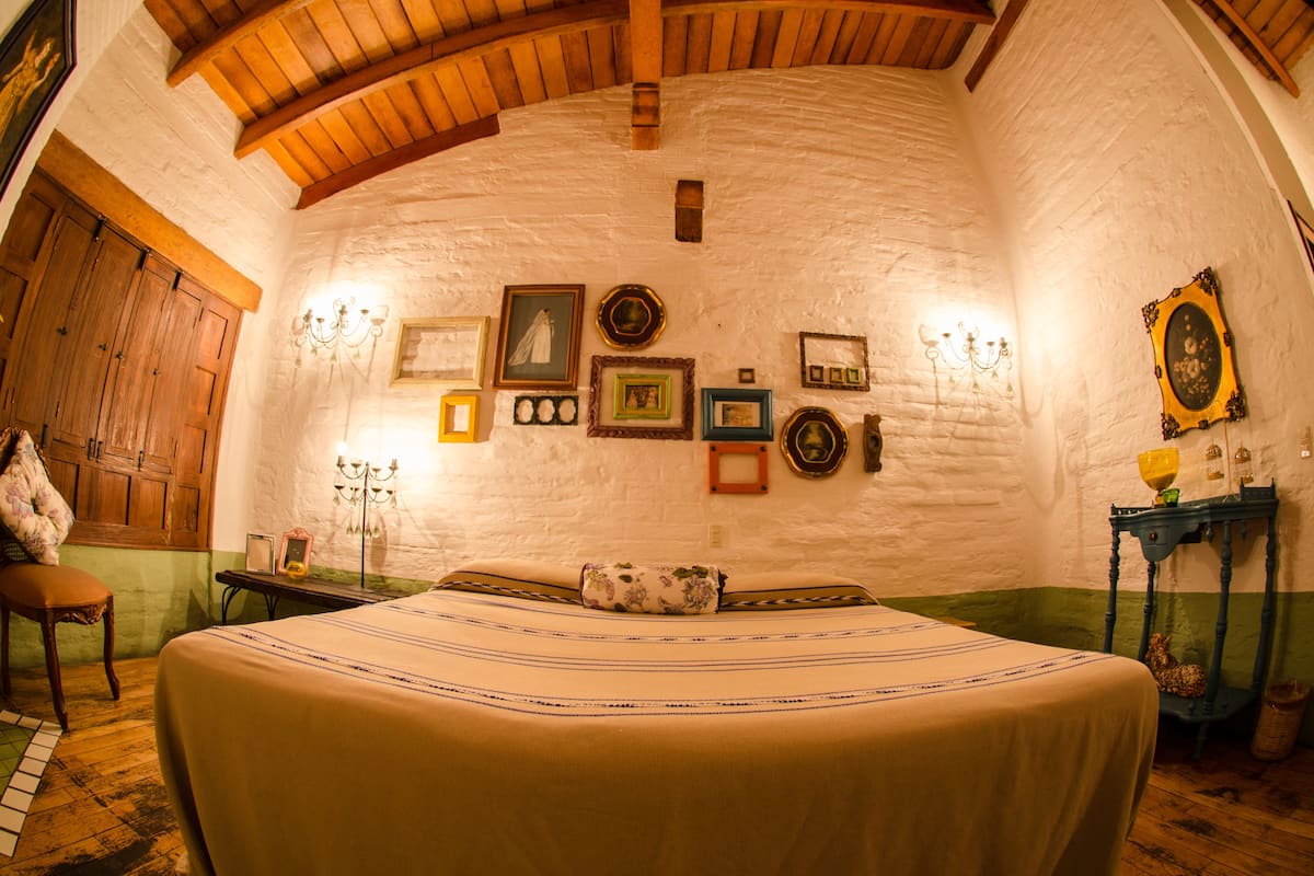 A cozy room with a bed, wooden ceiling beams, and a rustic wall with framed pictures.