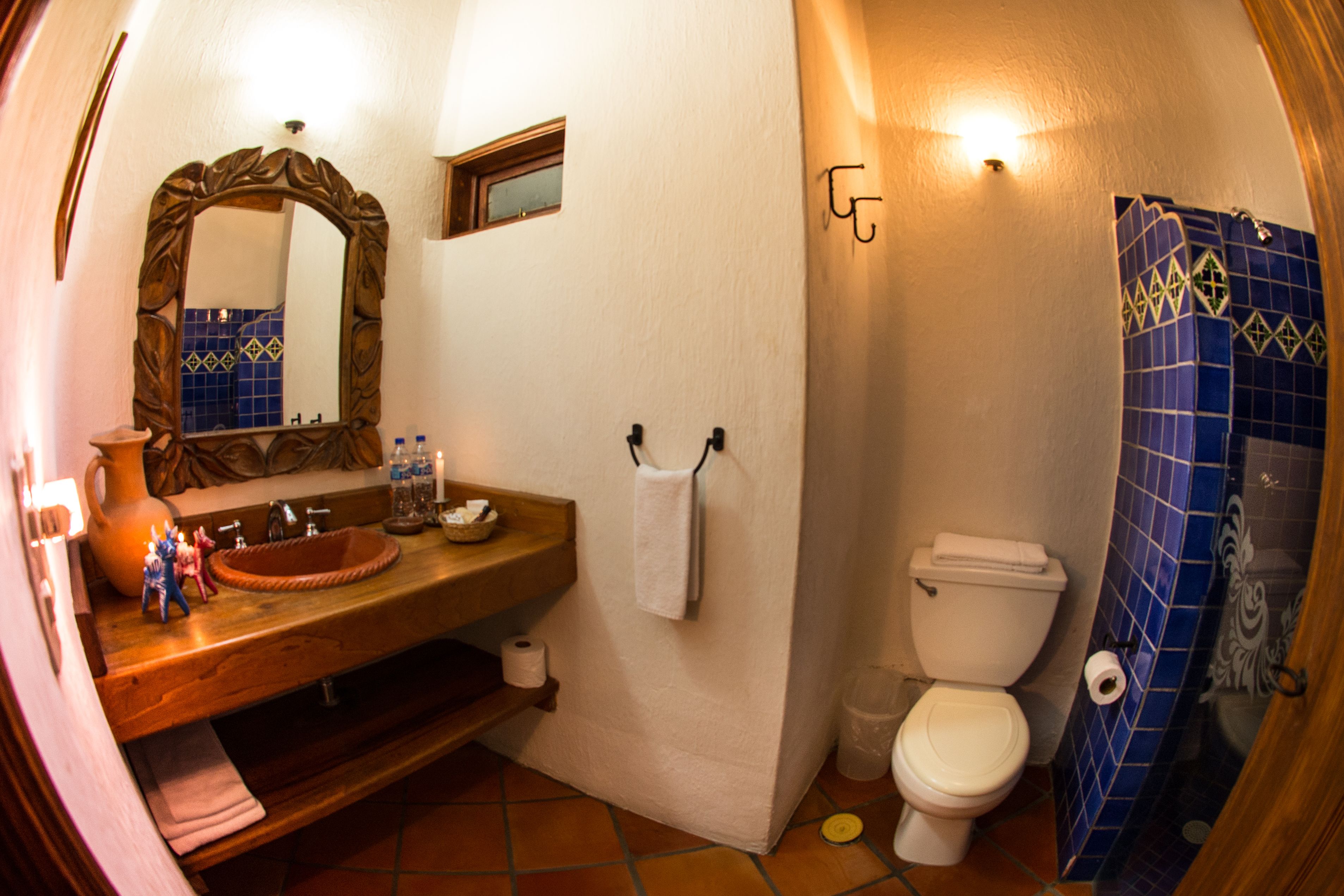 A bathroom with a wooden vanity, a large mirror, a white toilet, and a shower area with blue tiles.