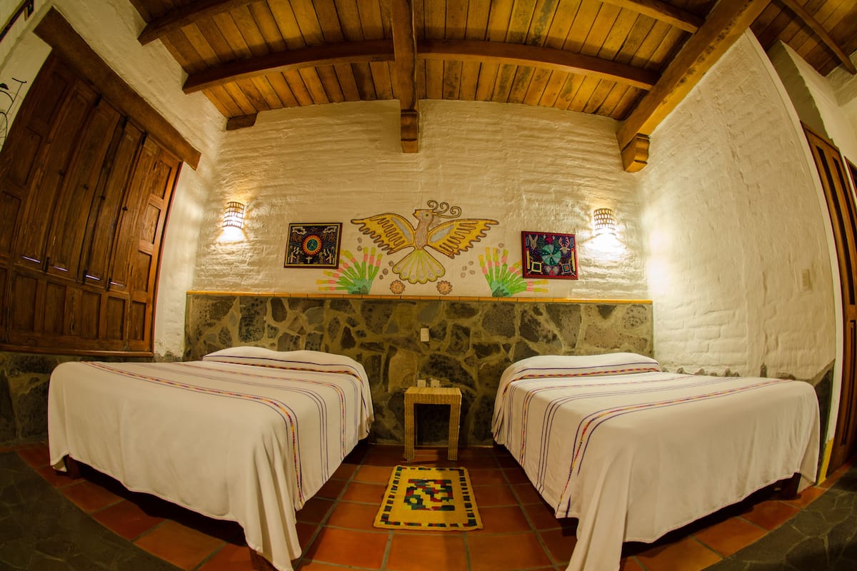 A room with two beds, a stone wall, wooden beams, and artwork on the wall.