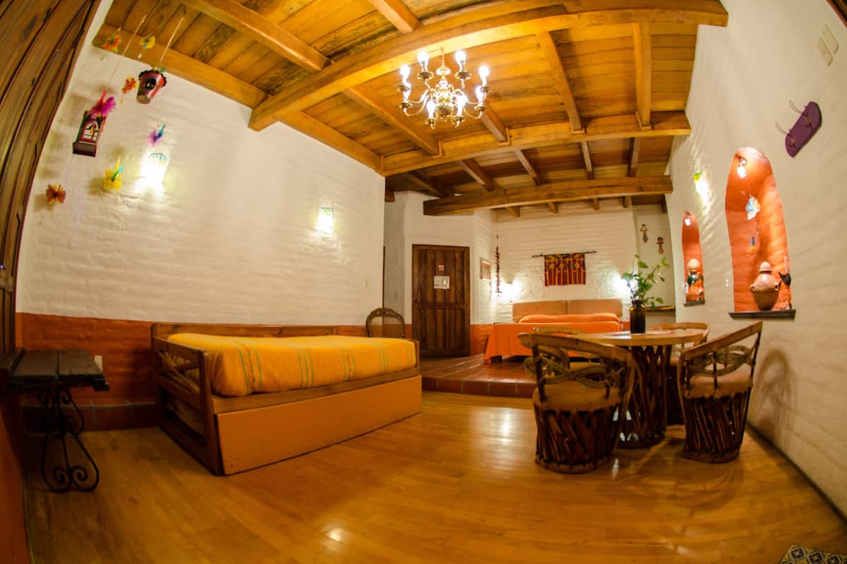 A cozy room with a wooden ceiling, a sofa, a dining table with chairs, and a small kitchen area.