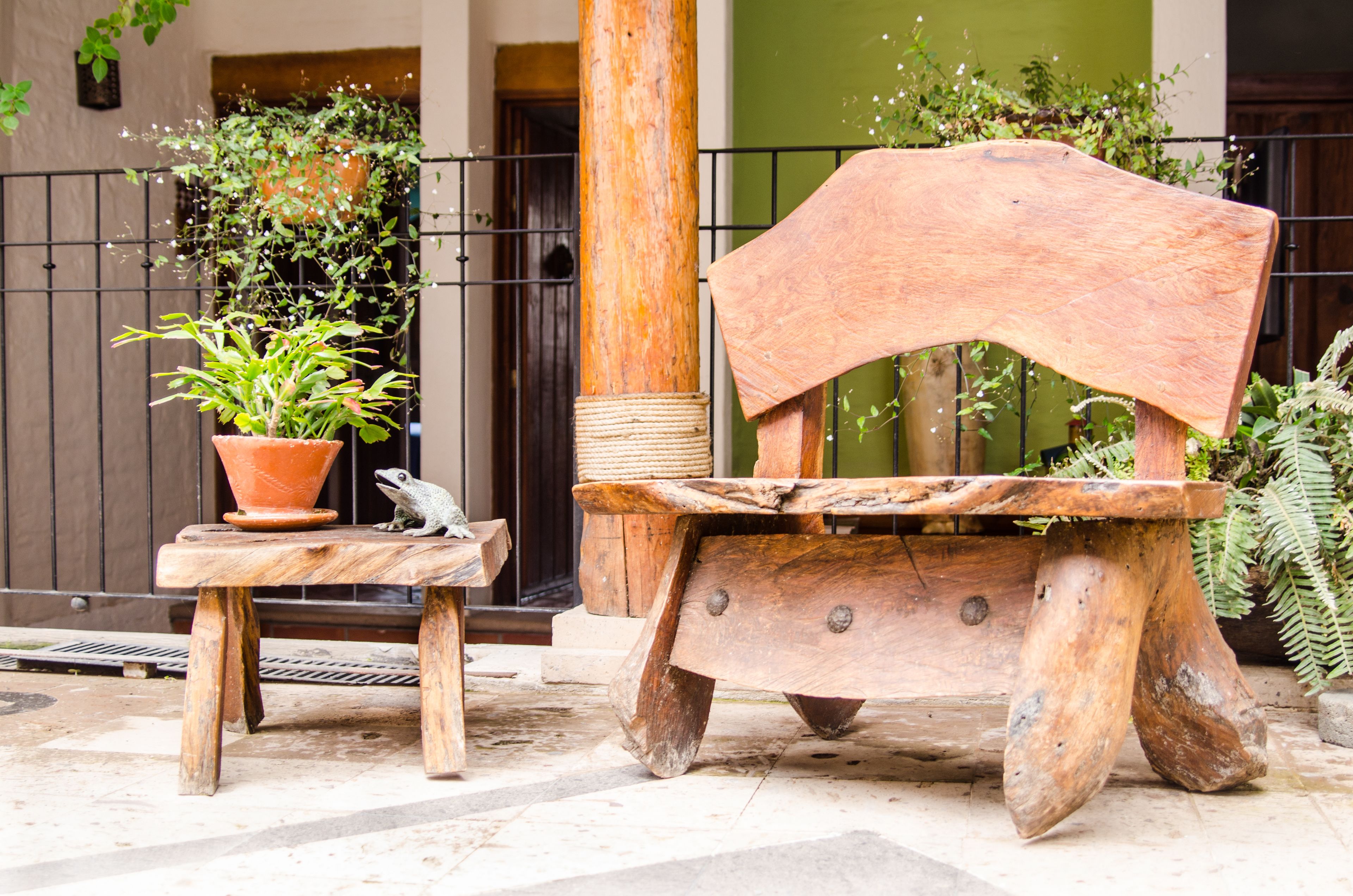 A rustic outdoor seating area with a wooden bench and a small table, surrounded by potted plants and a metal fence.