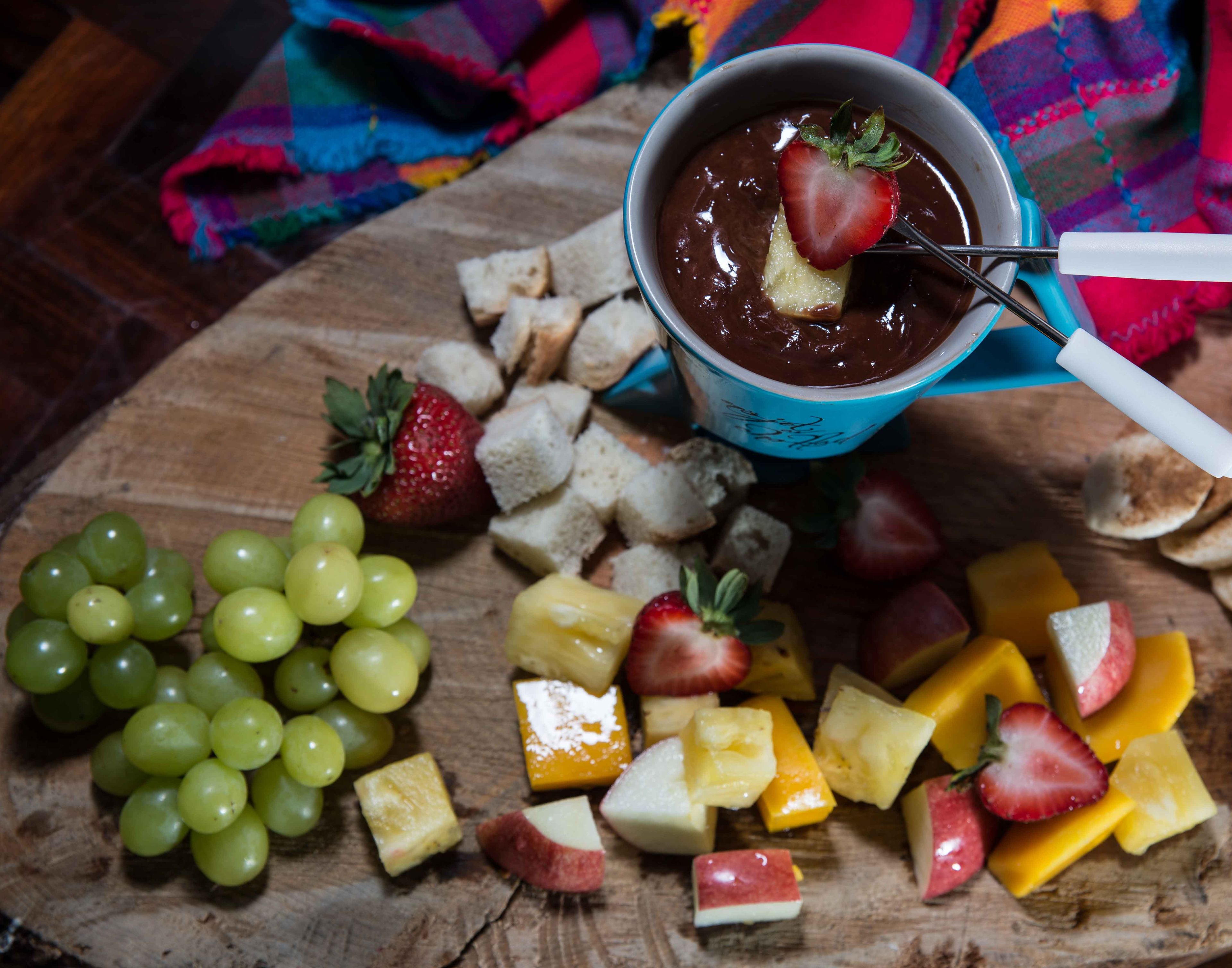 Une planche en bois sur laquelle sont disposés divers fruits, ainsi qu’un dessert au chocolat servi dans une tasse bleue.