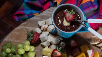 Une planche en bois sur laquelle sont disposés divers fruits, ainsi qu’un dessert au chocolat servi dans une tasse bleue.