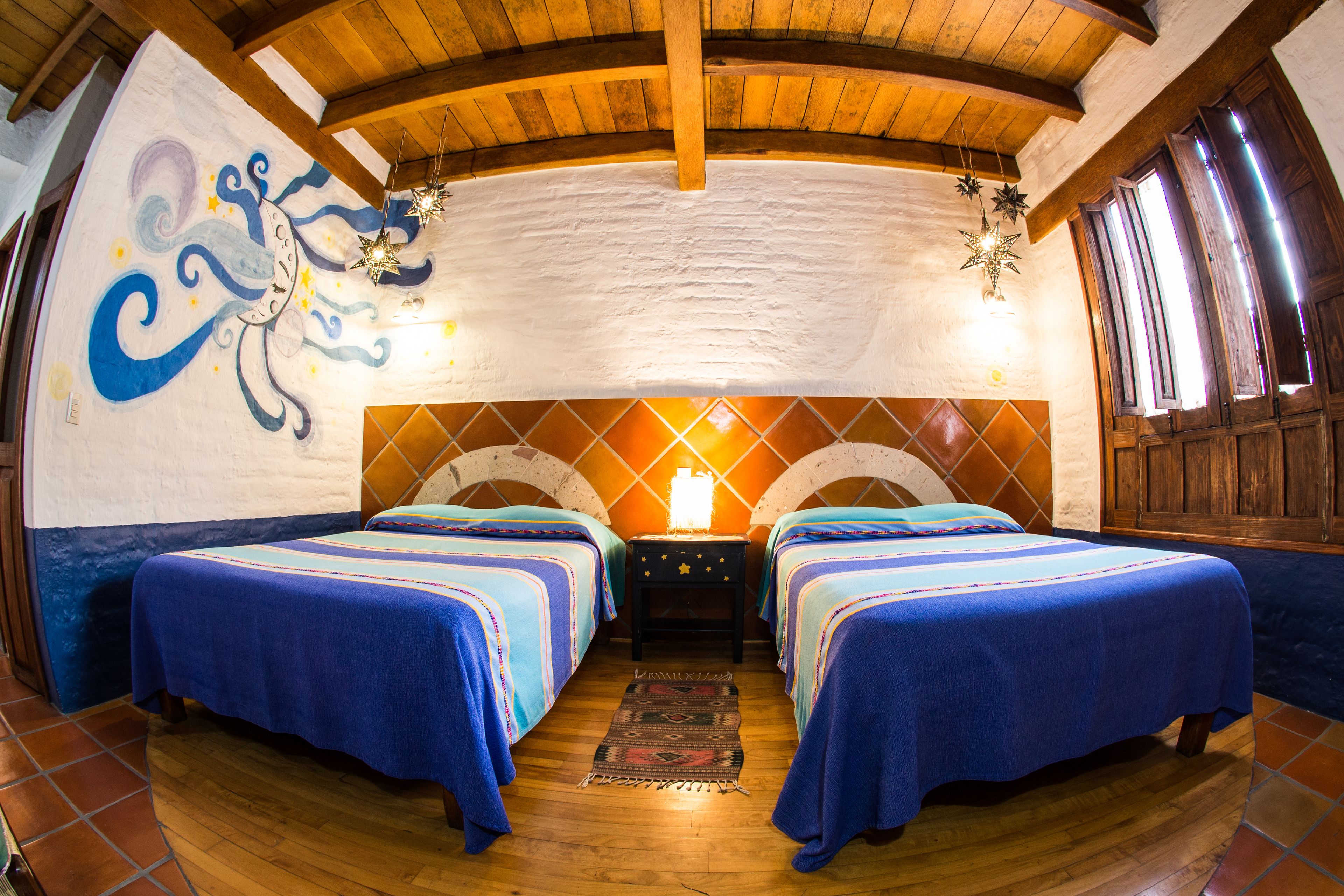 A room with two beds, a mural on the wall, and a wooden ceiling.