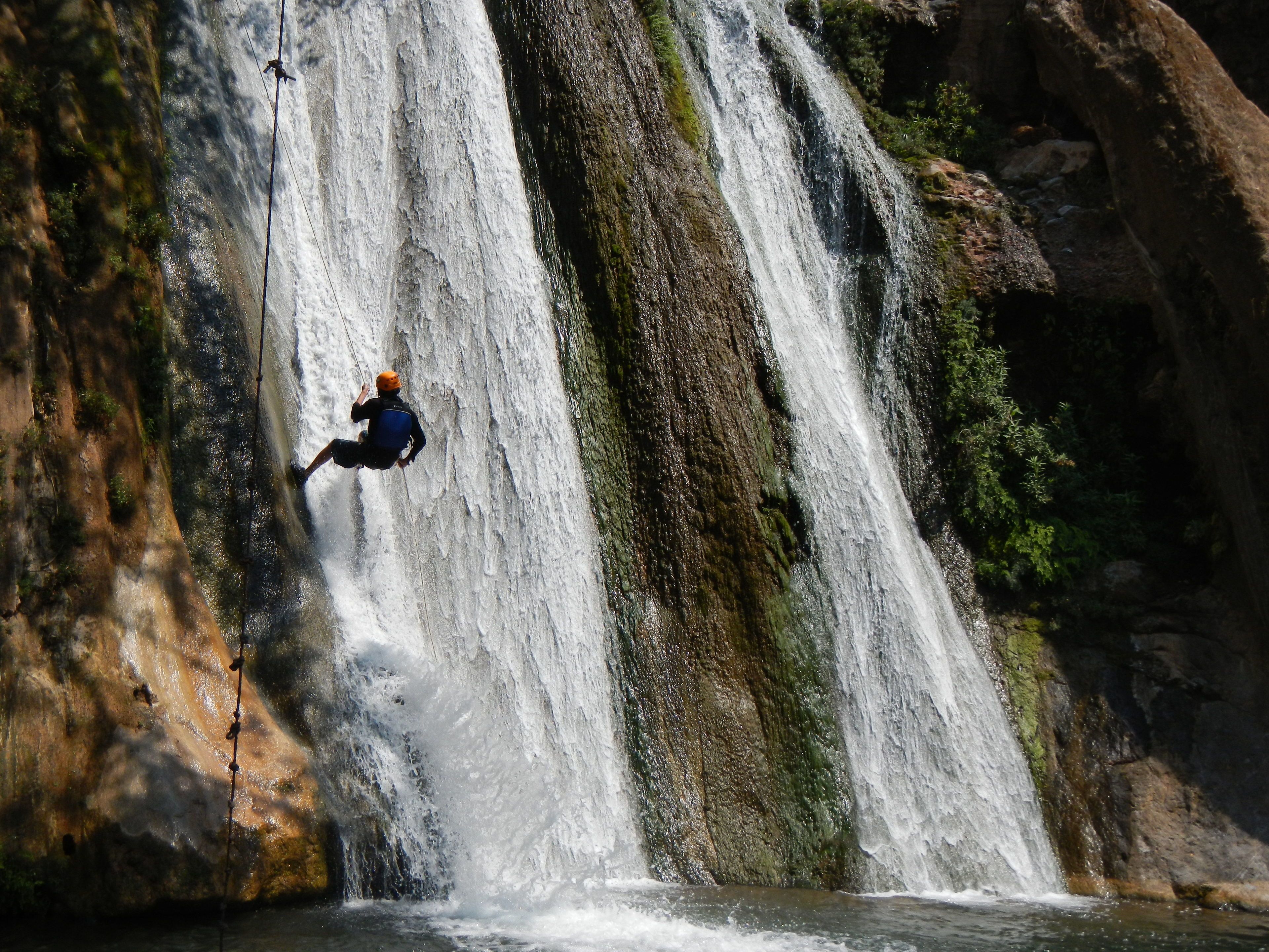 Una persona descendiendo en rápel por una cascada enorme.