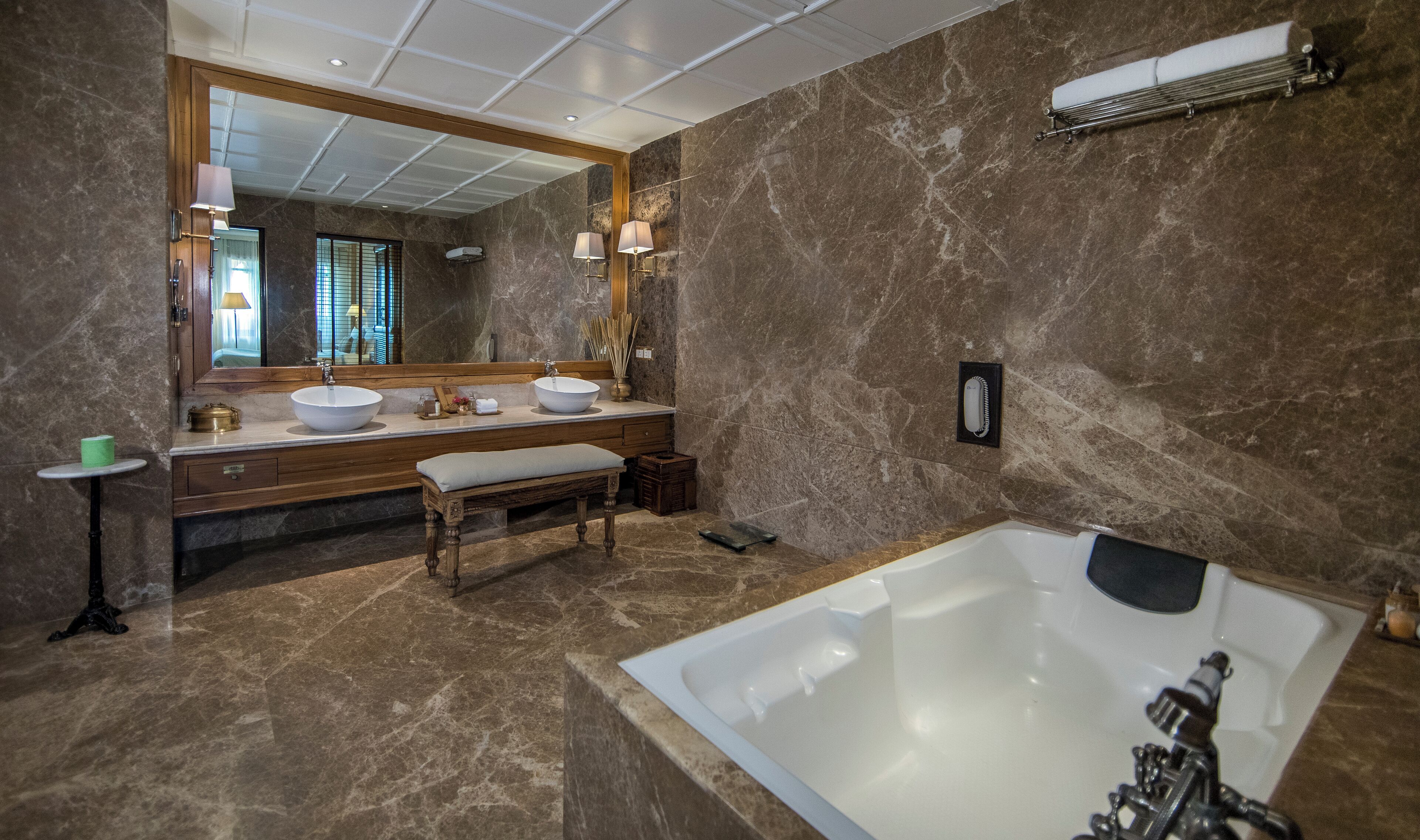 A modern bathroom with a large bathtub, two sinks, a bench, and a large mirror.