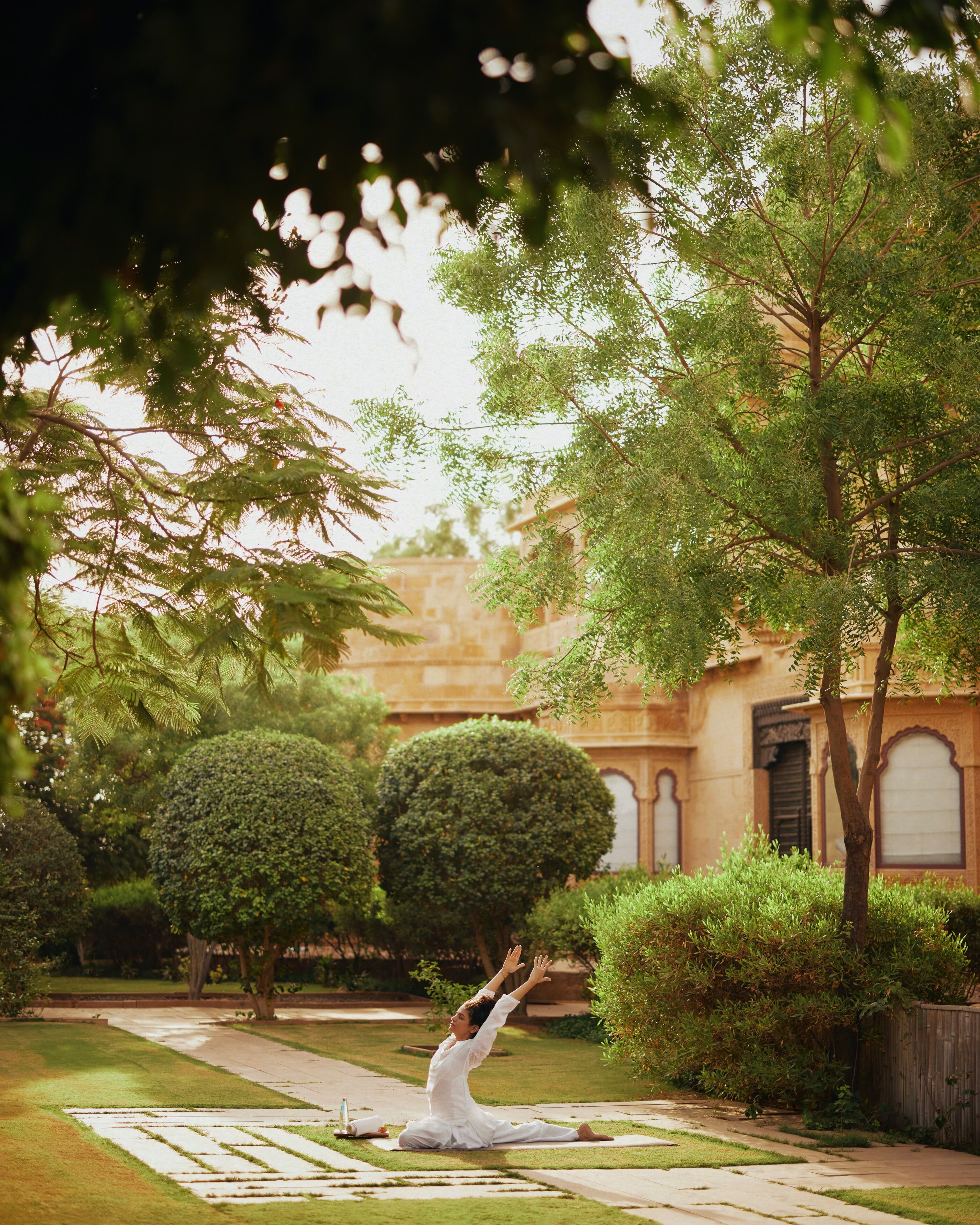A person practicing yoga in a garden with a building in the background.