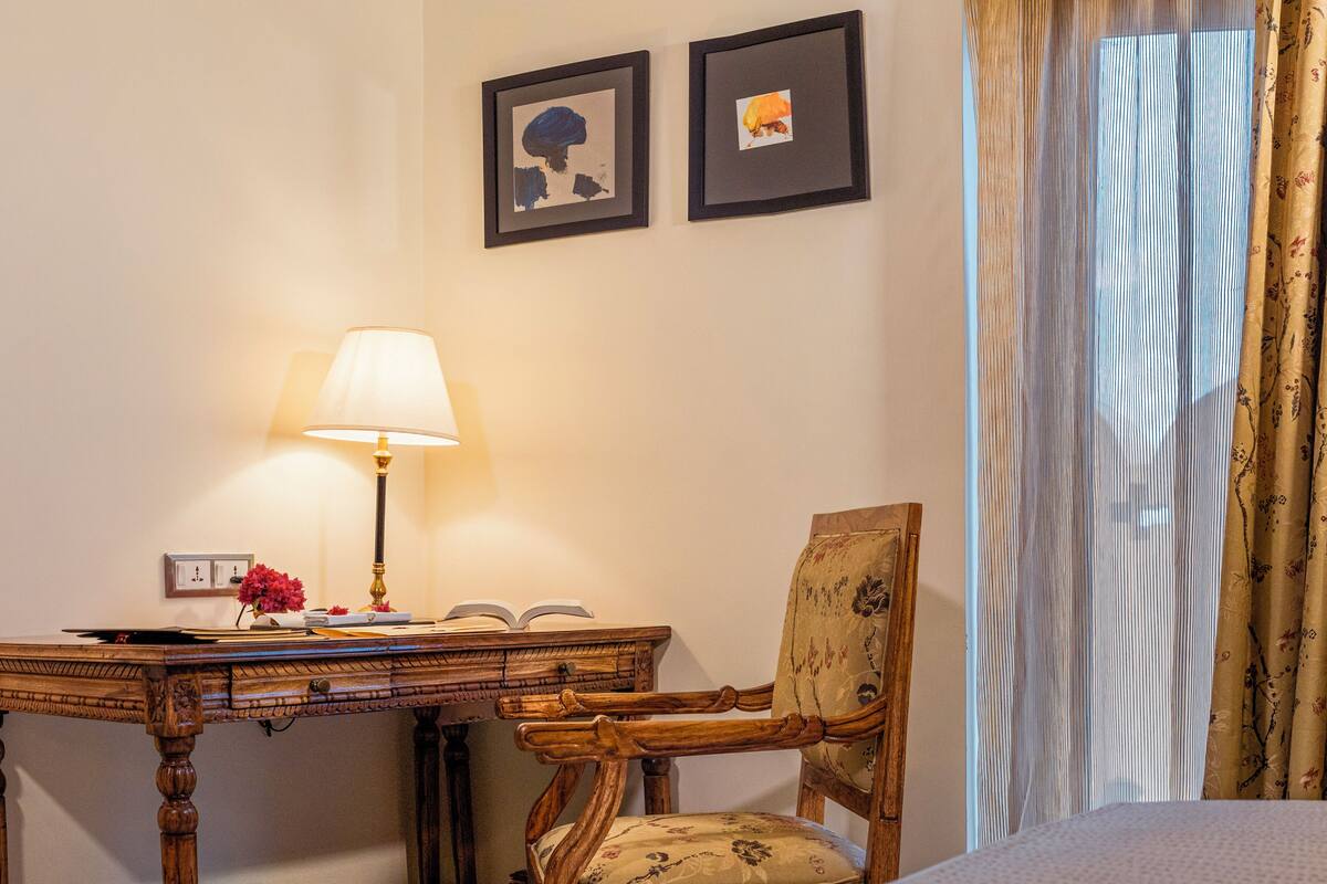 Habitación de hotel con un escritorio de madera, una silla, una lámpara y dos cuadros en la pared.