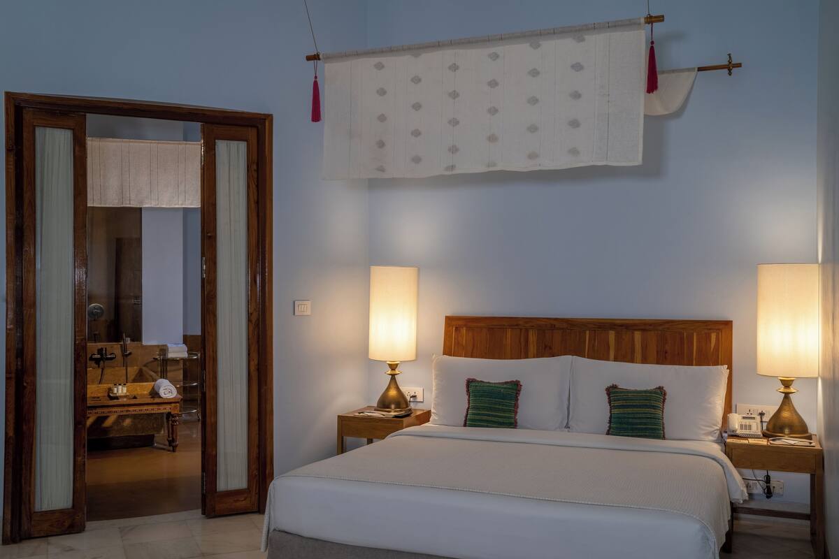 Habitación de hotel con una cama, dos lámparas de noche, un cabecero de madera y una cortina colgada.