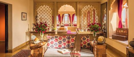 A traditional room with a sofa, a wooden side table, a patterned rug, and a view through a window with a decorative arch.