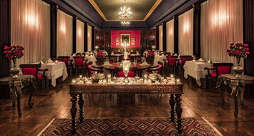 A formal dining room with multiple tables and chairs, a chandelier, and red accents on the walls.