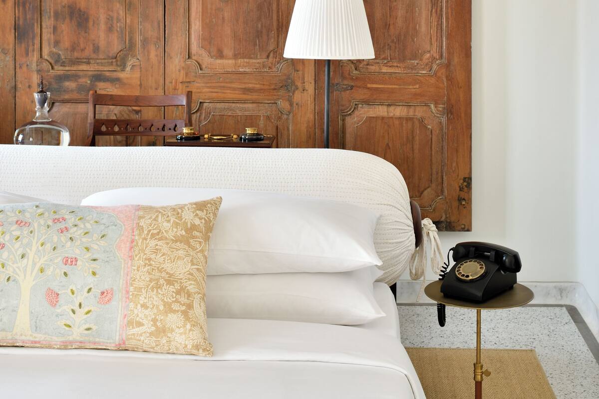 Habitación de hotel con pared de paneles de madera, cama con ropa blanca, lámpara, teléfono y alfombra.