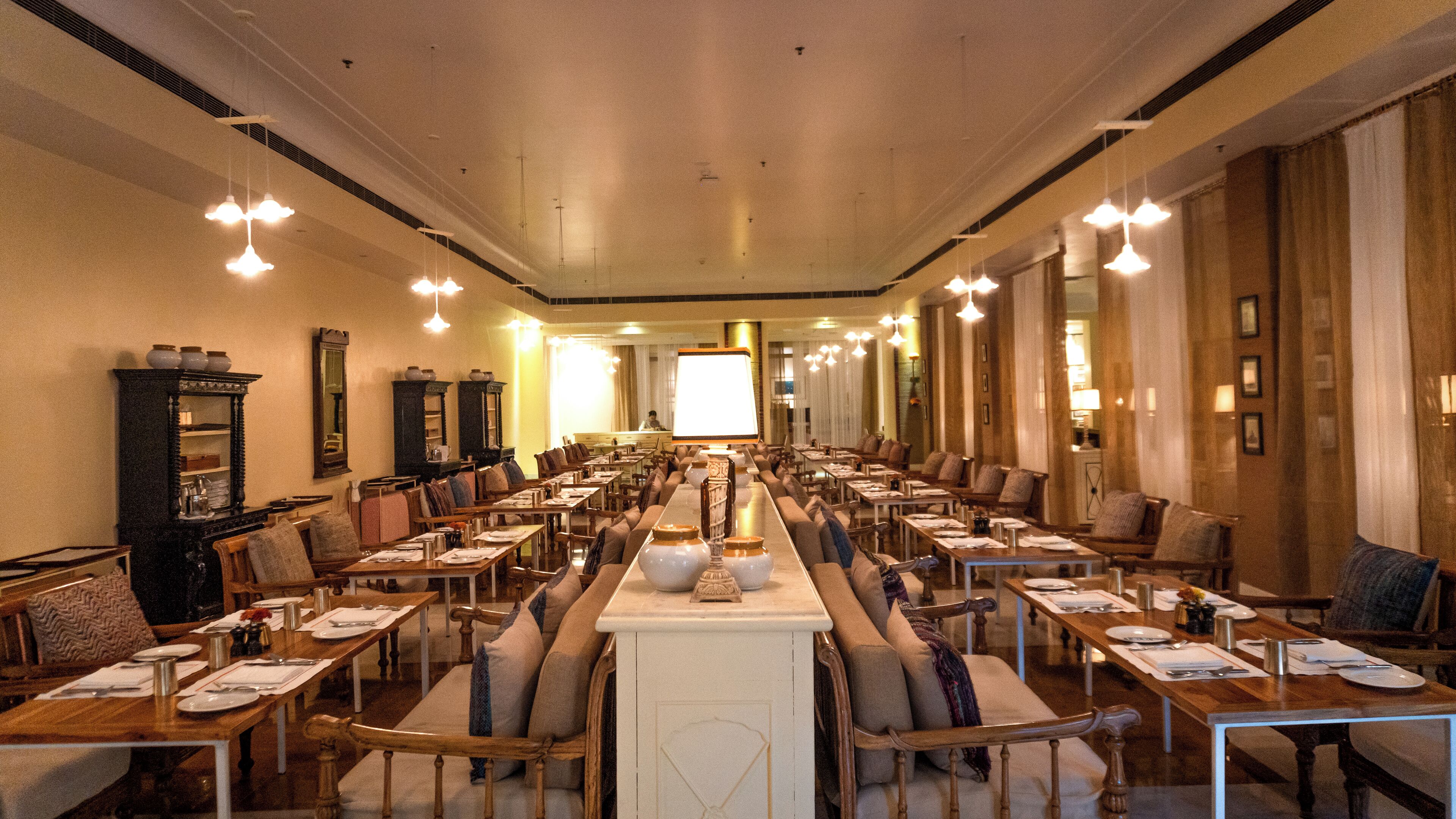 A spacious dining hall with long tables, chairs, and hanging lights.