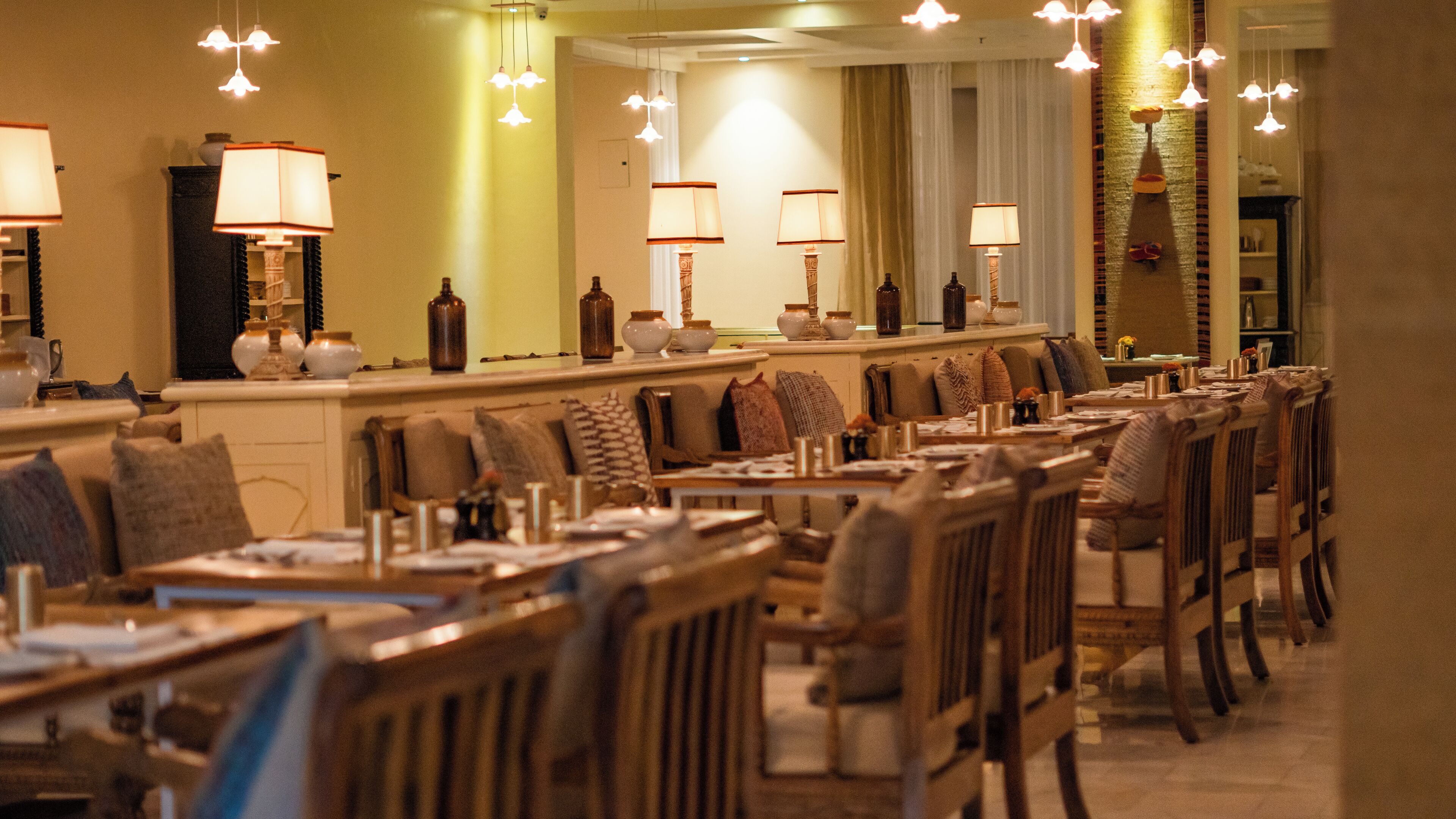 A hotel dining area with multiple tables and chairs, overhead lighting, and a counter with a mirror.