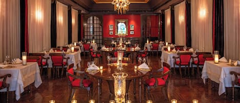 Un comedor formal con mesas dispuestas para varios invitados, un candelabro y velas sobre la mesa central.
