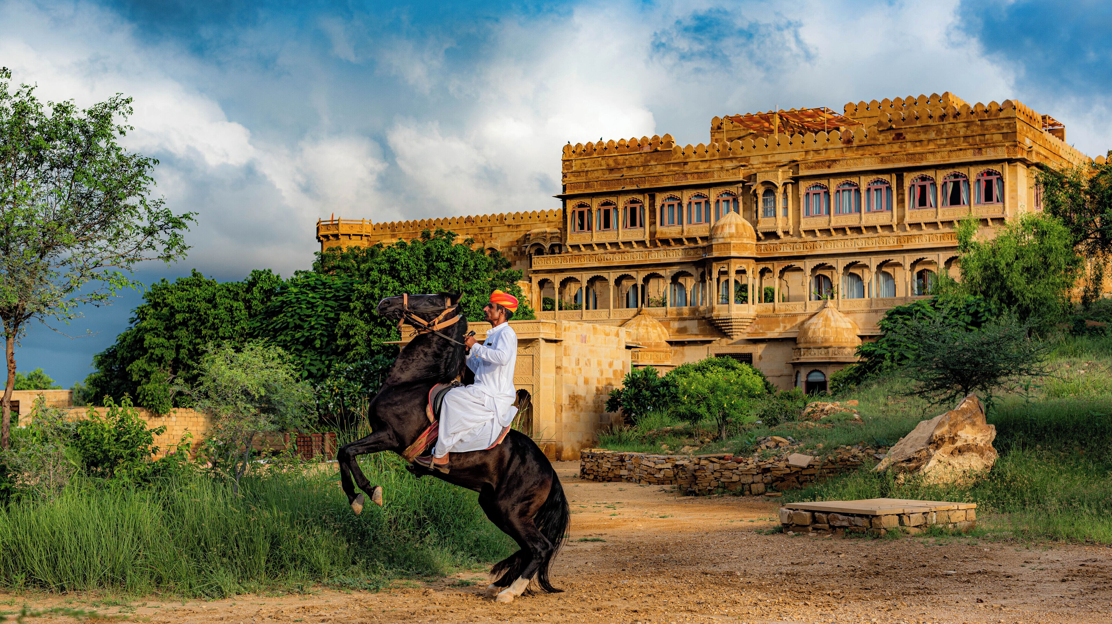 Un homme à cheval devant un grand bâtiment orné, doté de nombreuses fenêtres et de coupoles.