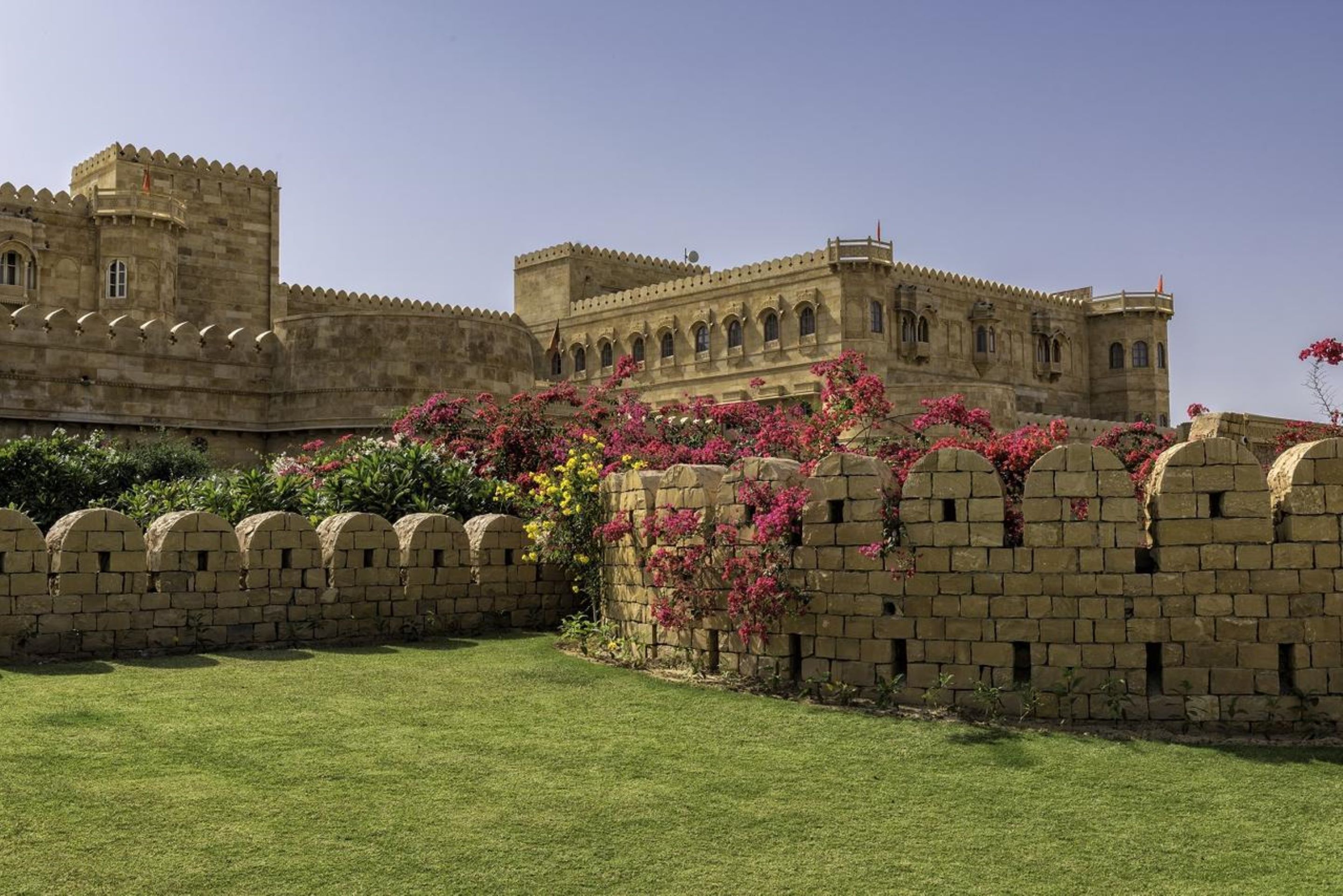 A historic building with a fortified wall and arched windows, surrounded by a well-maintained lawn.