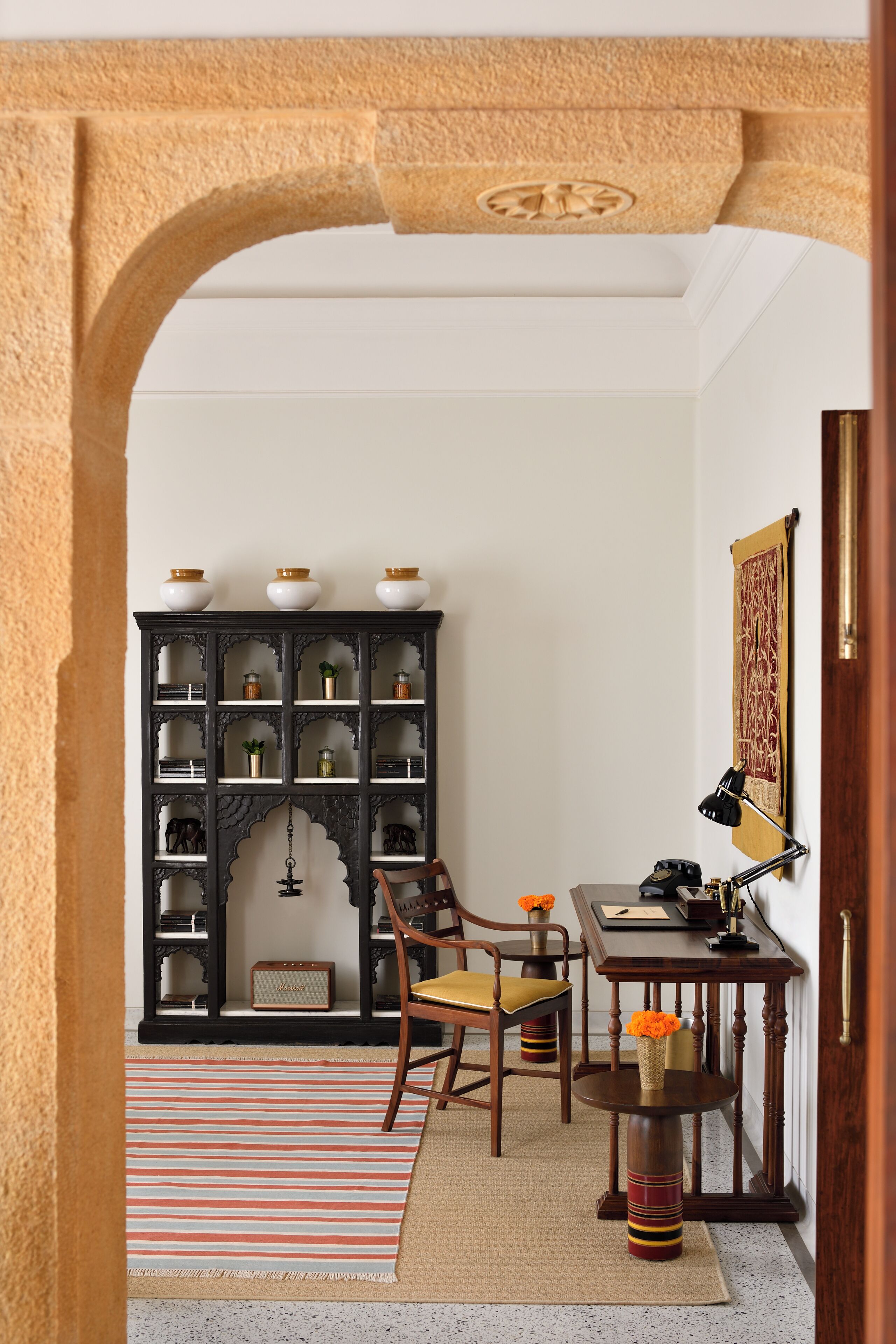 A room with a dark wooden bookcase, a small round table with a lamp, and a chair with a yellow cushion.