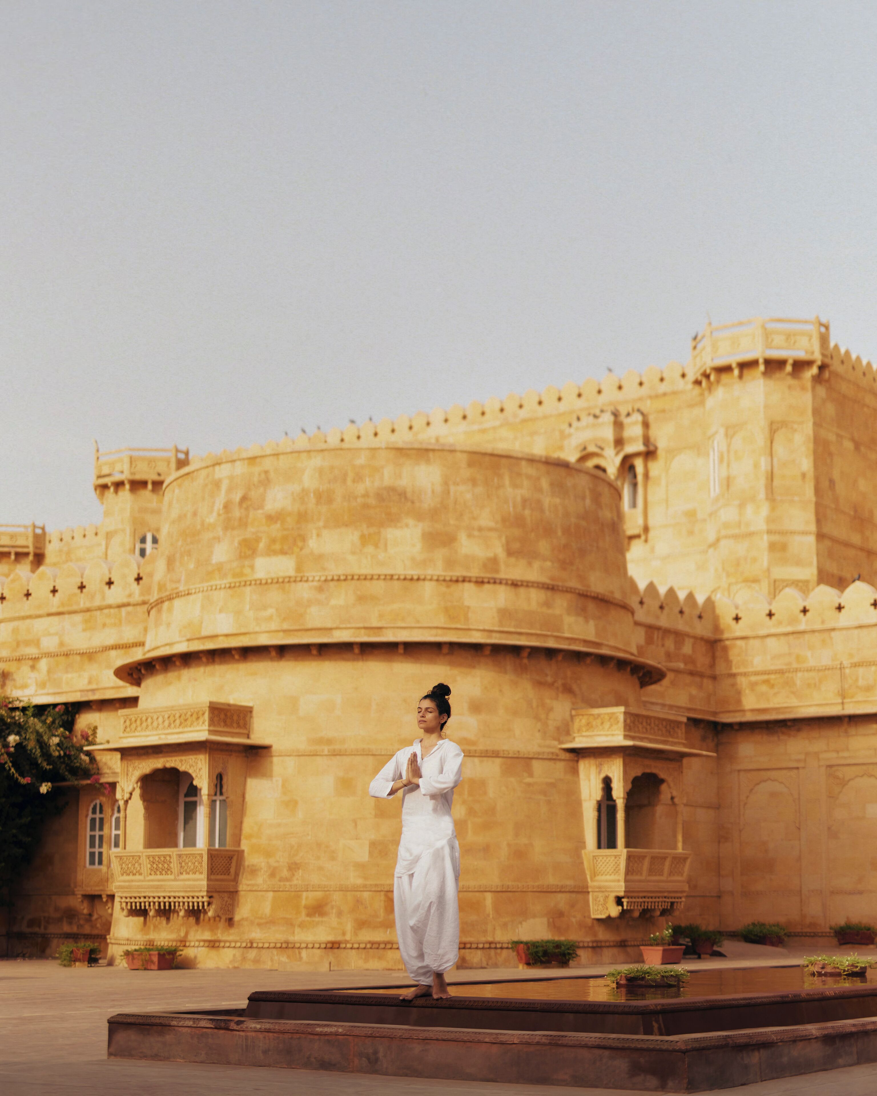 A person in traditional attire standing in front of a historic building with a large, round structure and detailed architecture.