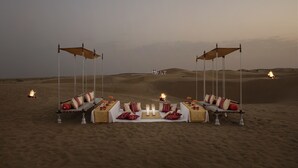 A desert dining setup with a central table, two swing seats, and a fire in the background. - Suryagarh (Jaisalmer)