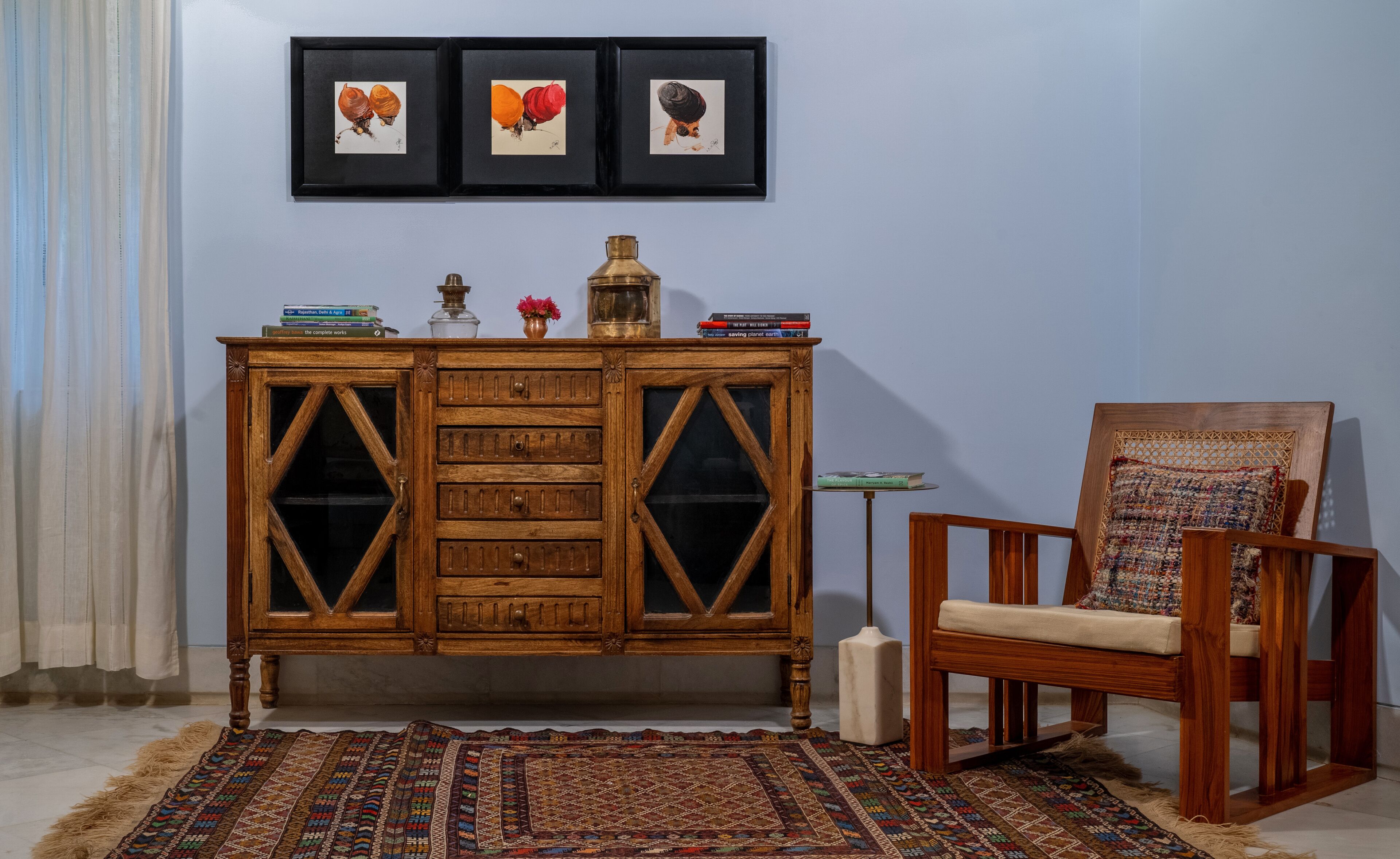 A room with a wooden cabinet, a chair, a rug, and three framed pictures on the wall.