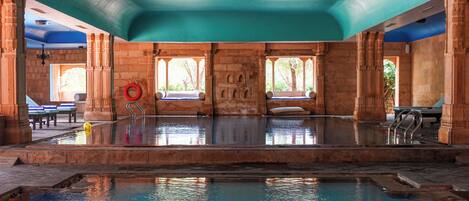 A large indoor swimming pool with stone architecture, benches, and a lifebuoy.