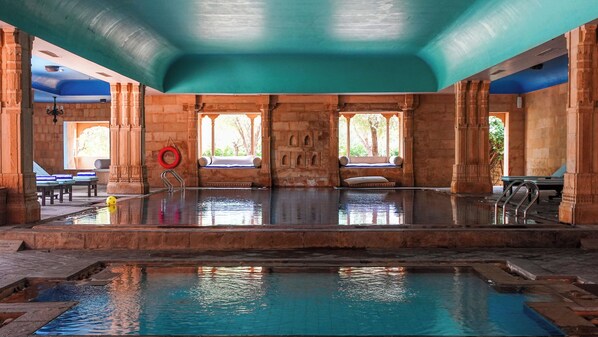 A large indoor swimming pool with stone architecture, benches, and a lifebuoy.