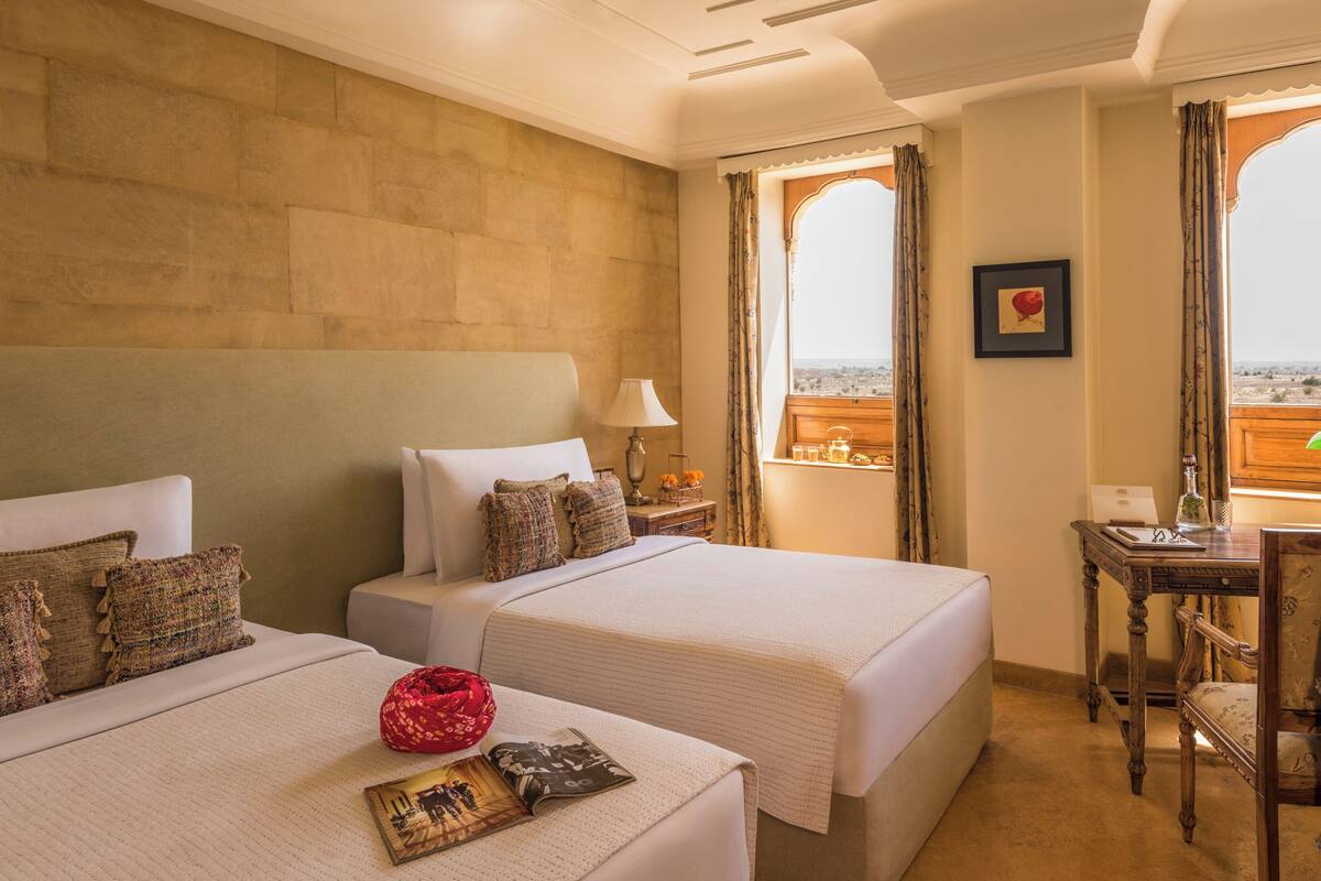Habitación de hotel con dos camas, un escritorio, una silla y vistas al paisaje desértico.